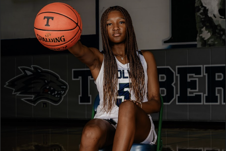 The image shows a young woman with long braided hair holding a basketball in a basketball court setting.