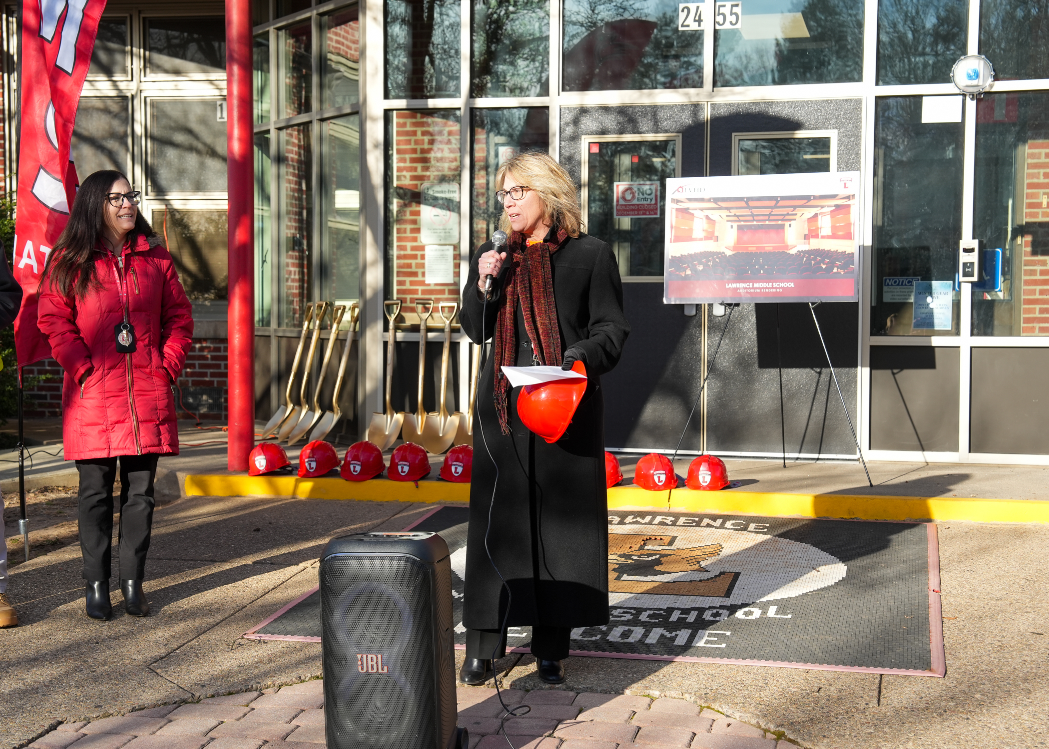 Two women, one wearing a red coat and the other a black coat, stand in front of a storefront with various items displayed in the window.