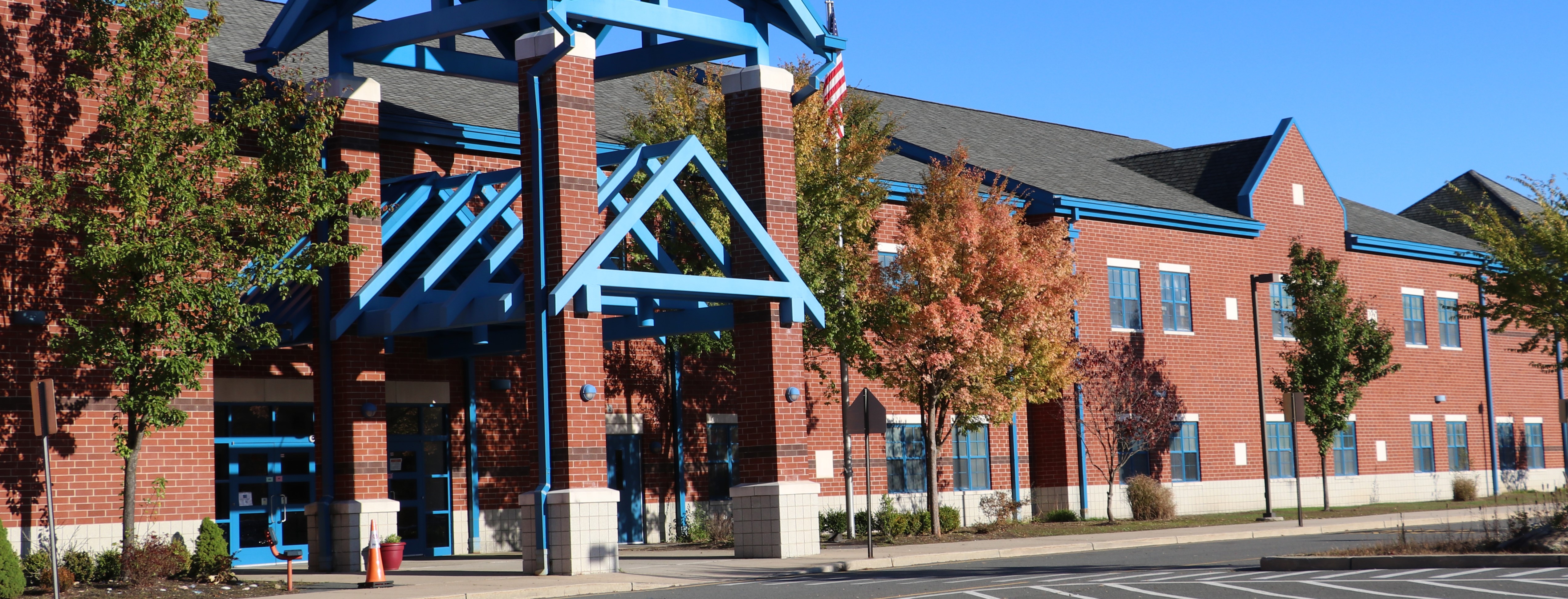 A modern brick building with a distinctive architectural design, featuring a mix of geometric shapes and patterns, surrounded by trees and a clear blue sky.