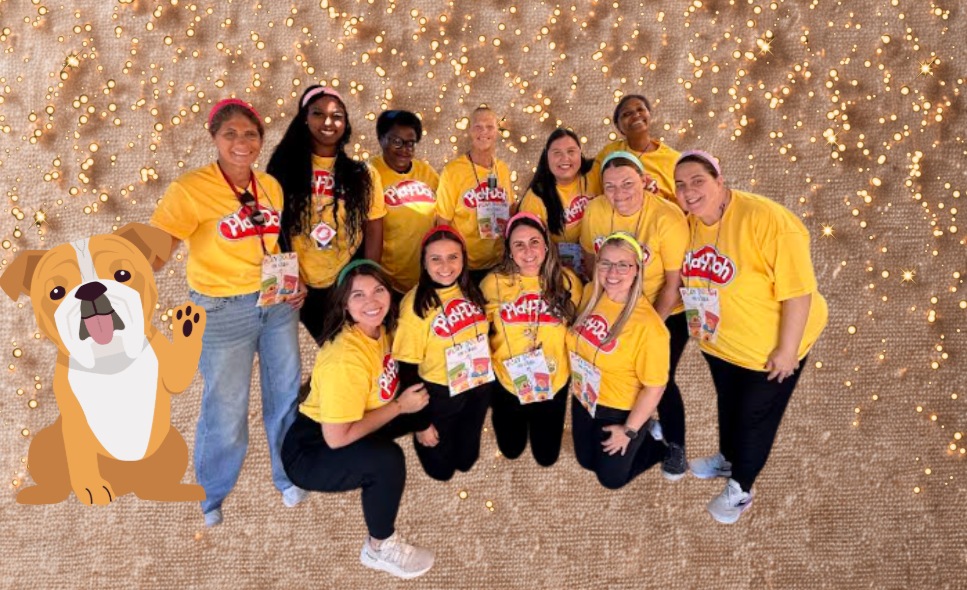 A group of women in yellow shirts stand in front of a sparkly gold background, with a cartoon bulldog waving in the foreground.