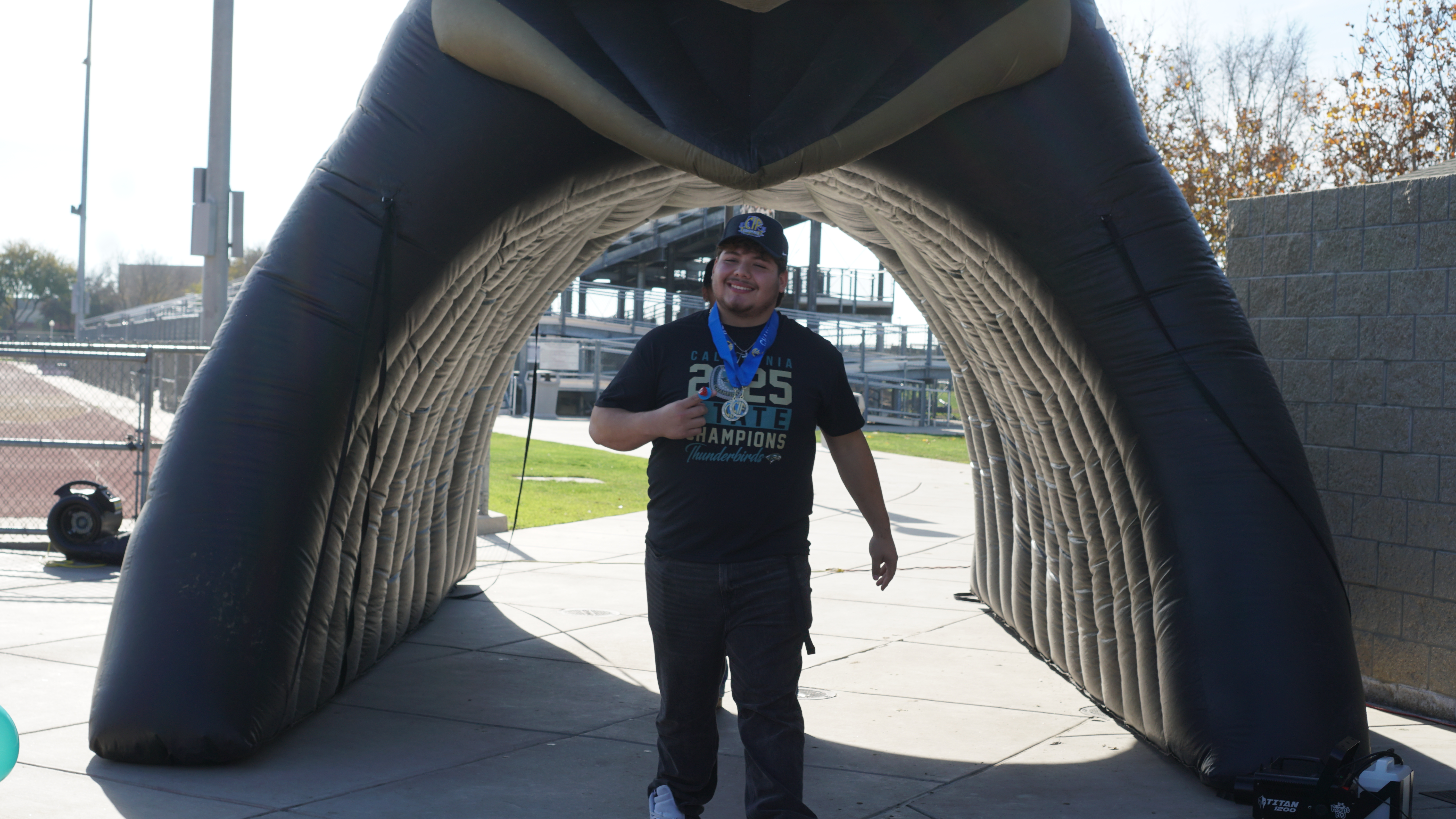 A person wearing a black shirt and pants stands in an archway-like structure with a curved, textured design in the background.