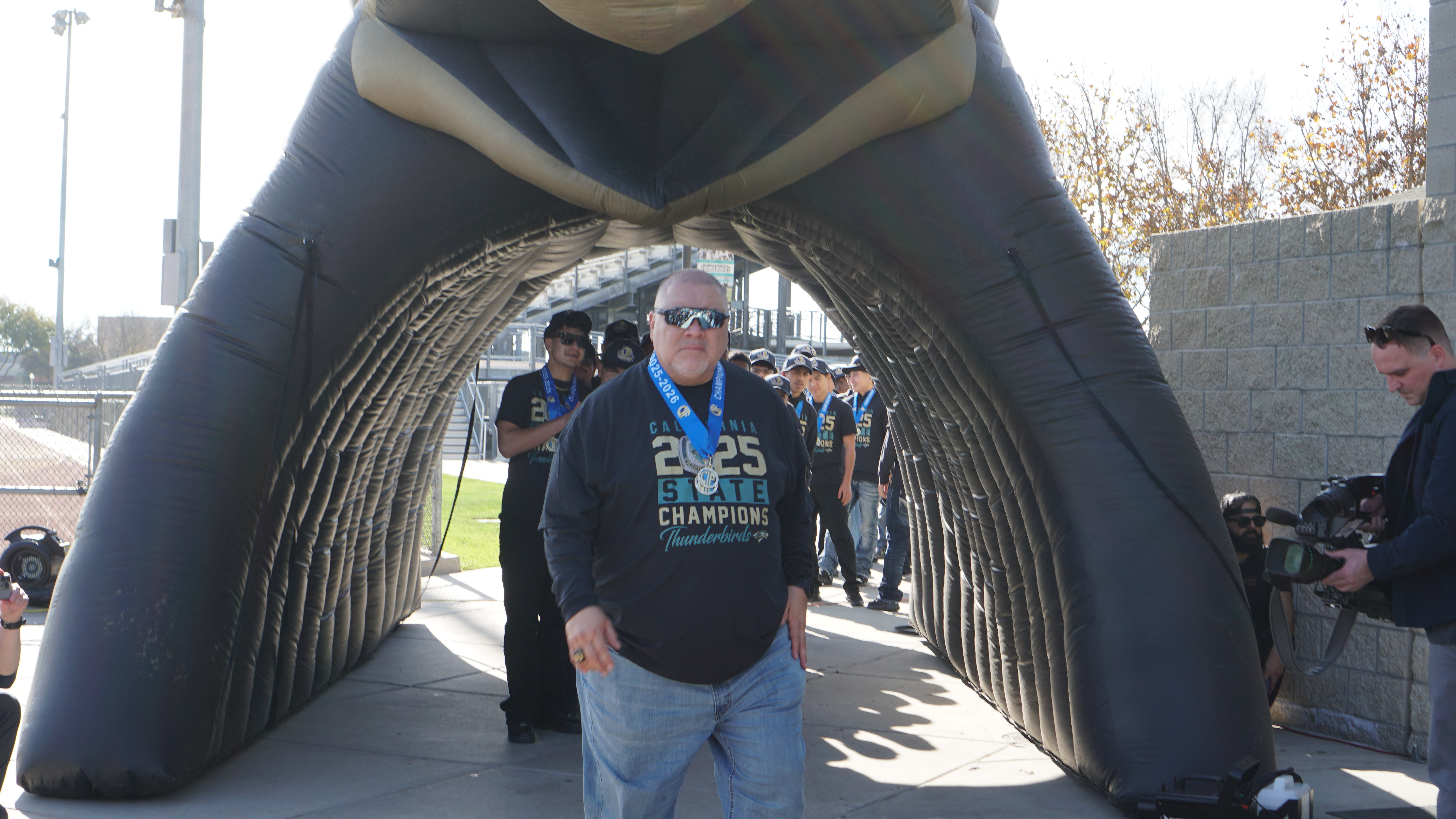 A large inflatable arch structure with a "2023 Champions" logo stands in the foreground, with a crowd of people visible in the background.