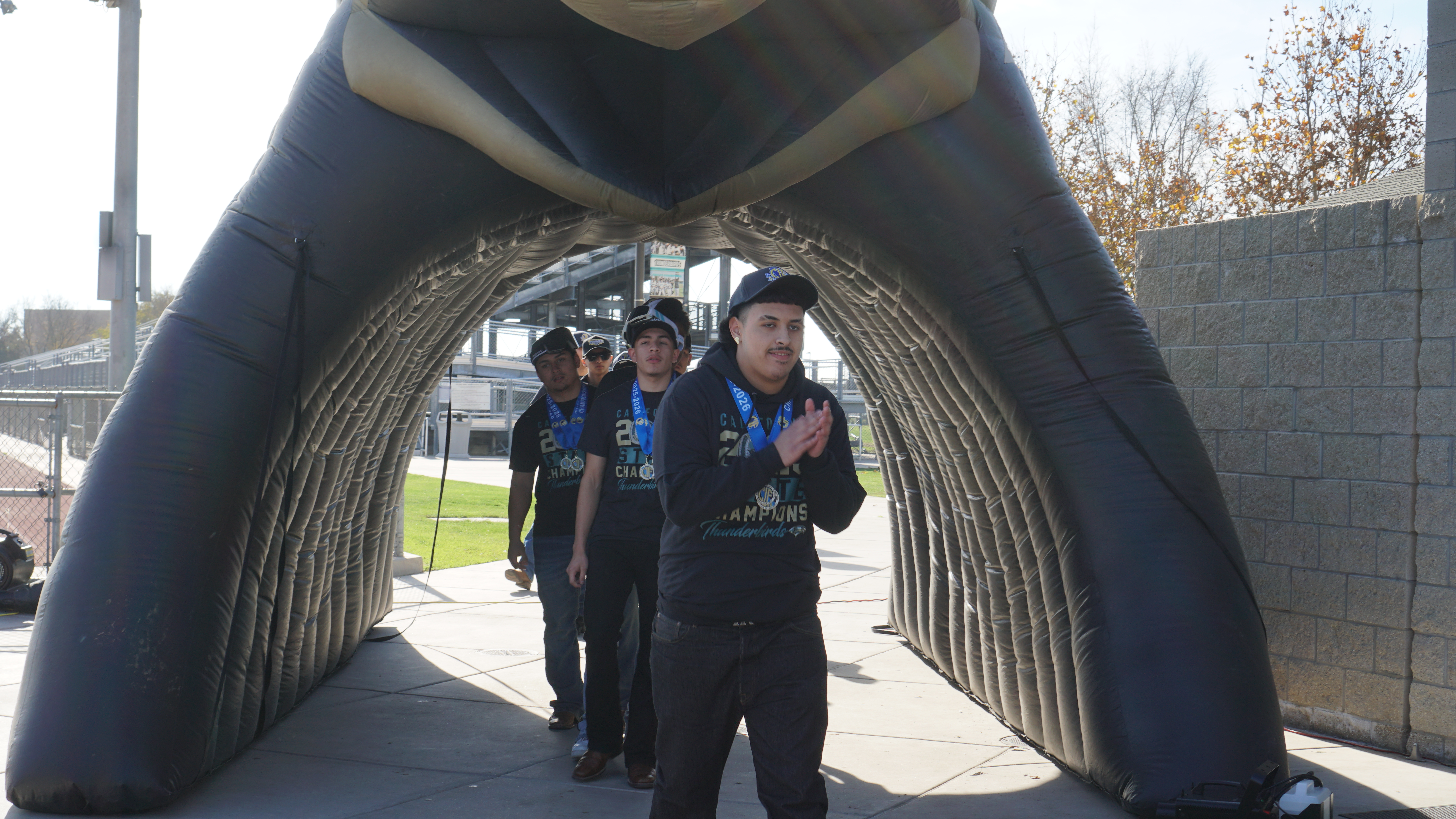 The image shows a group of people standing in an arched entryway, with a large black and white structure in the background.