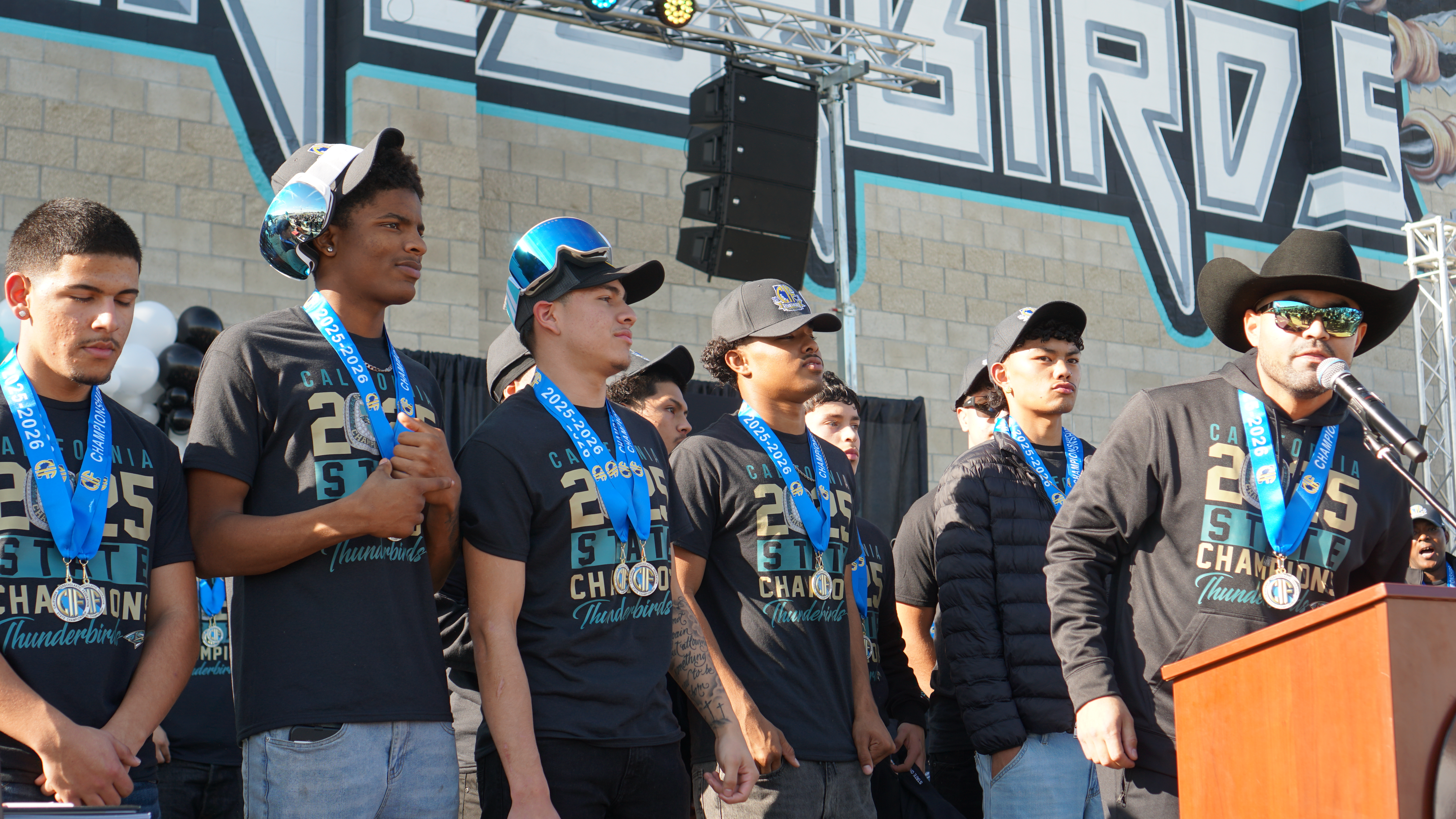 A group of young people, likely a sports team, standing in front of a colorful graffiti-covered wall, wearing matching jerseys and caps.