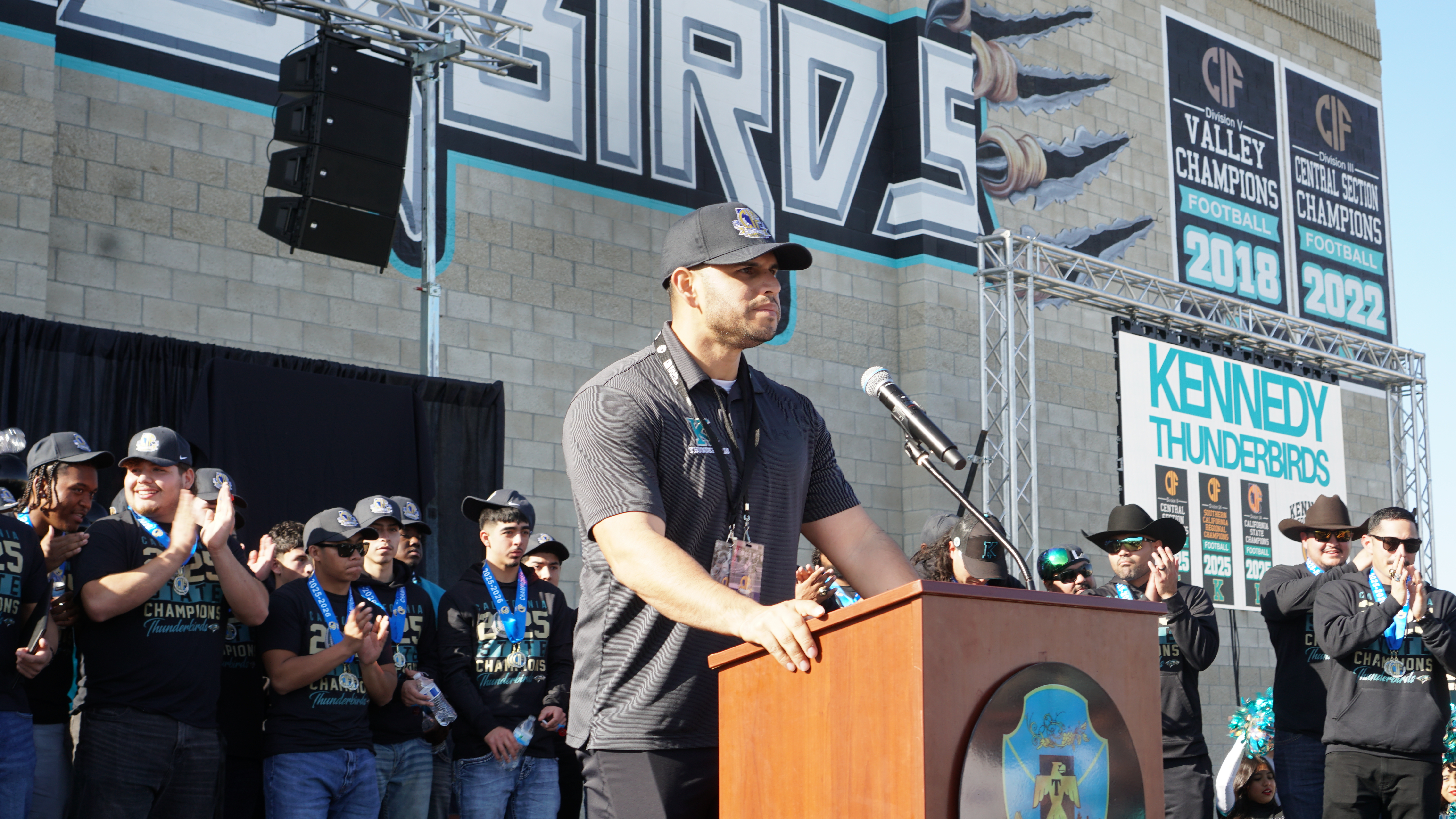 A man stands at a podium in front of a large crowd, with a stage and backdrop featuring the word "IRZE" visible in the background.