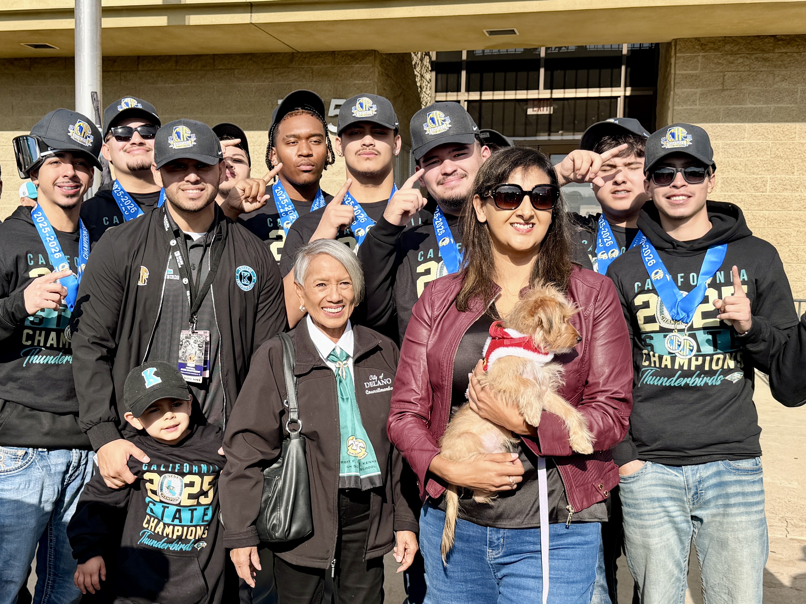 A group of people, some wearing championship shirts, posing together in front of a building.