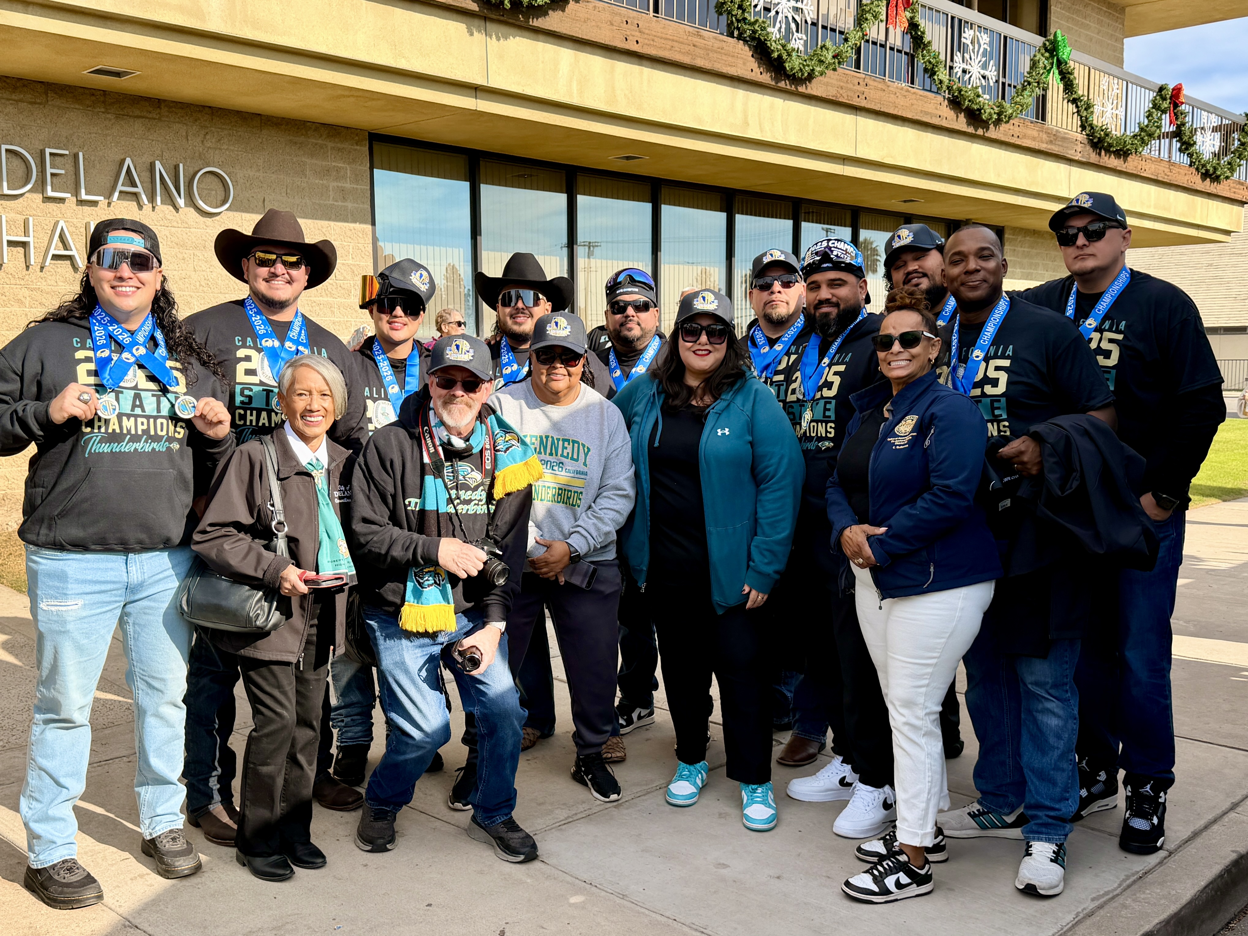 A group of people, some wearing cowboy hats, standing in front of a building with a sign that says "Delano Hall".
