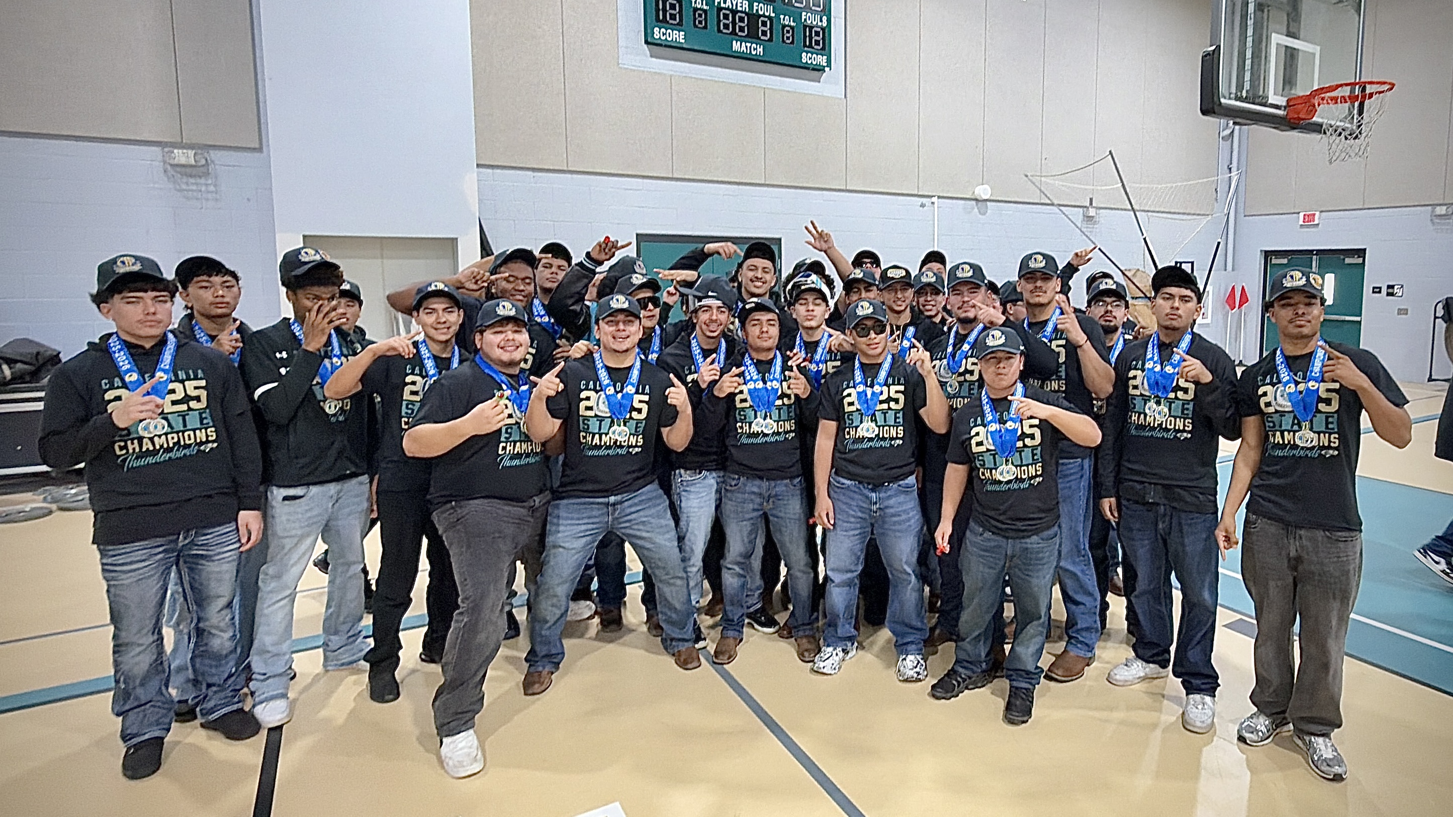 A group of young people, wearing matching black shirts with logos, are gathered together in a gymnasium-like setting, posing for a group photograph.
