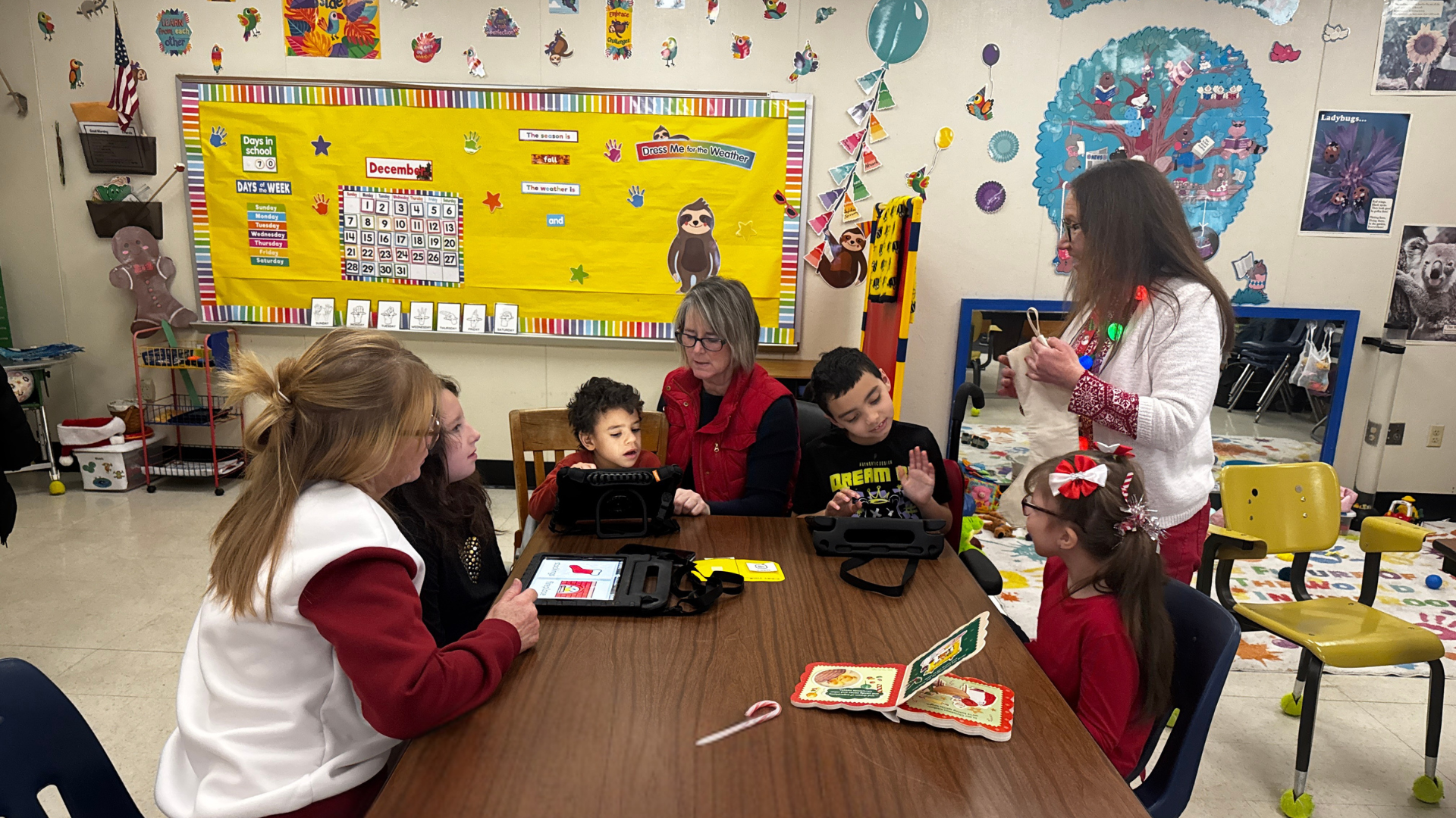 Teacher and paraprofessionals read a Christmas story to the class while students use iPads to communicate and identify items from the story.