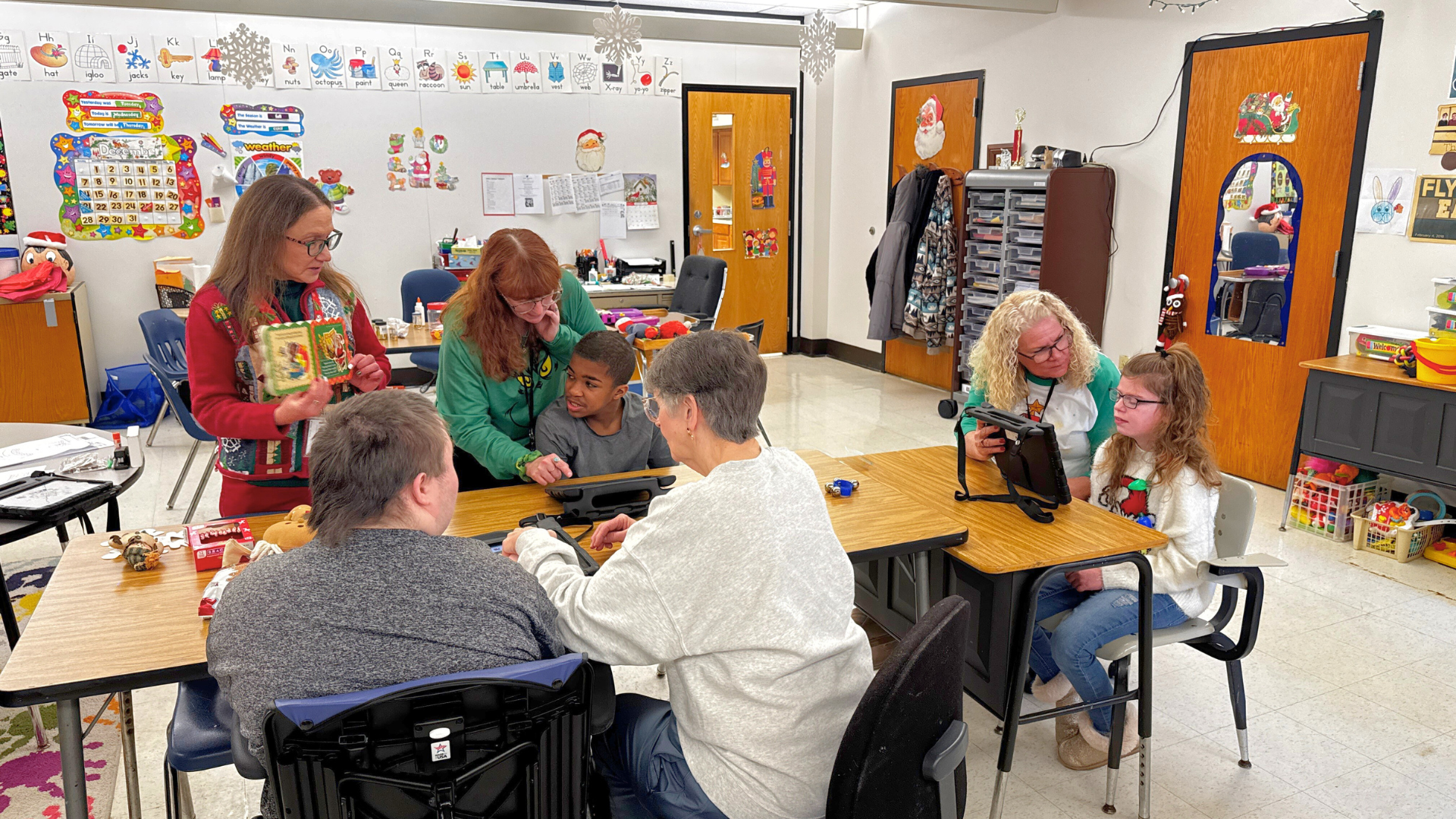 Teacher and paraprofessionals read a Christmas story to the class while students use iPads to communicate and identify items from the story.