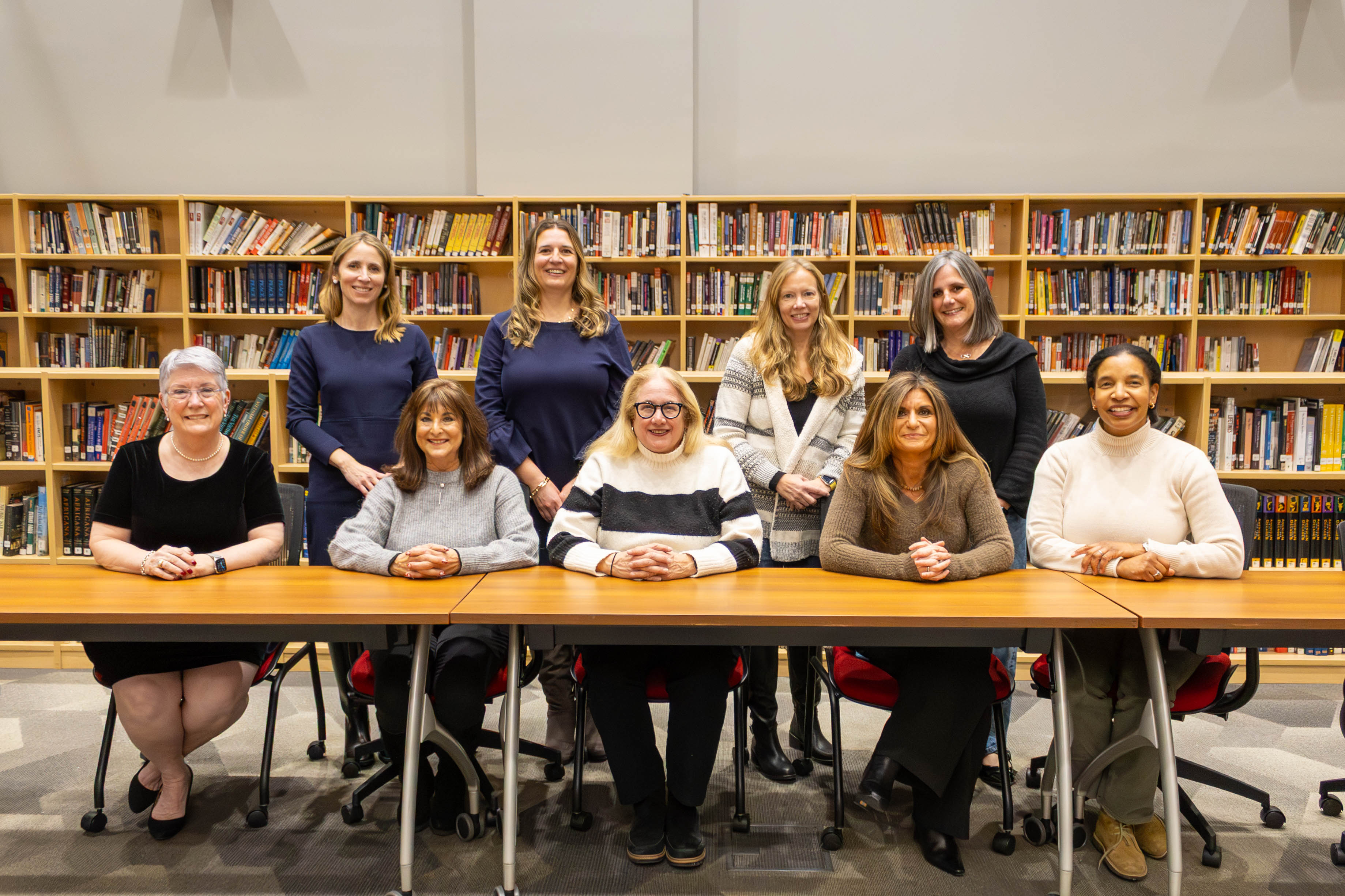 A group of women sitting at a table in a library setting, surrounded by bookshelves filled with books.