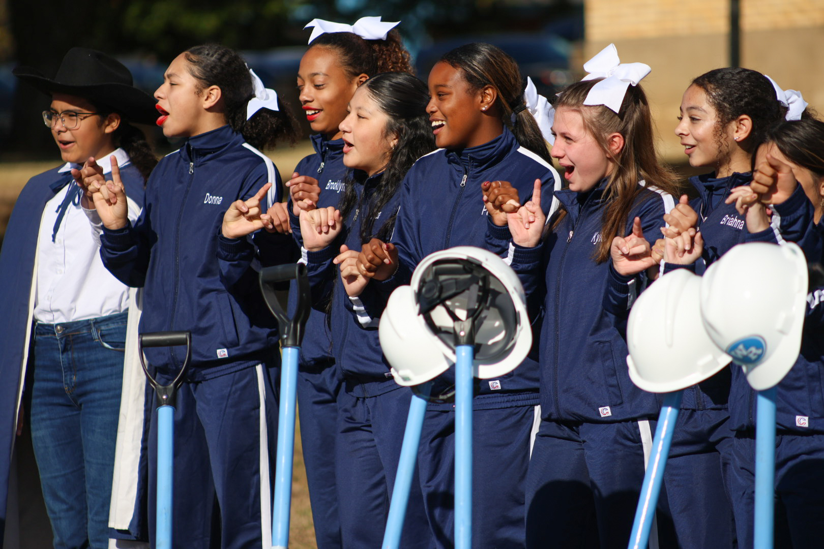 A group of young students, dressed in matching navy blue uniforms, are enthusiastically clapping and cheering while holding white fans.