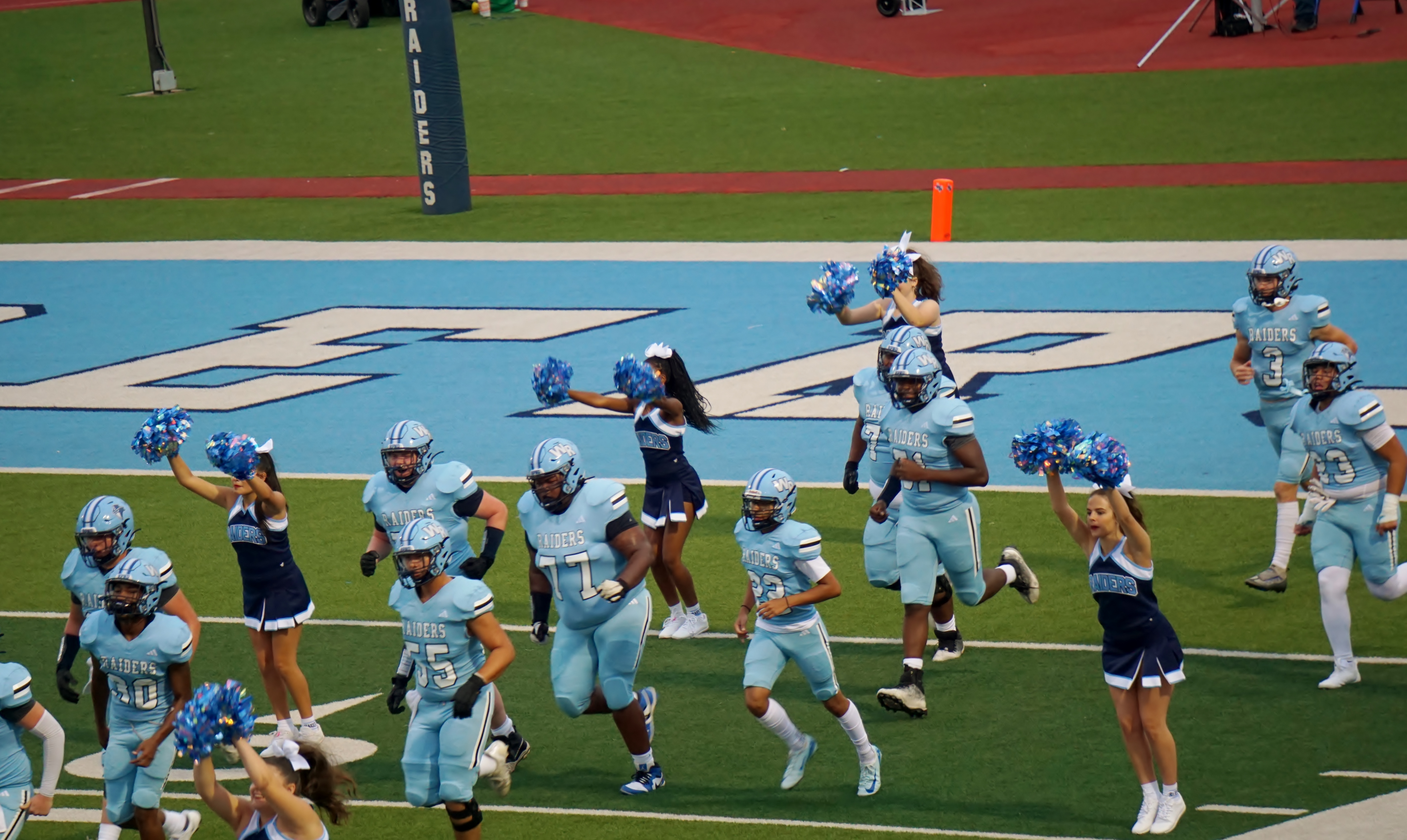 The image shows a group of football players in uniform on a football field, with a large "EAP" logo visible in the background.