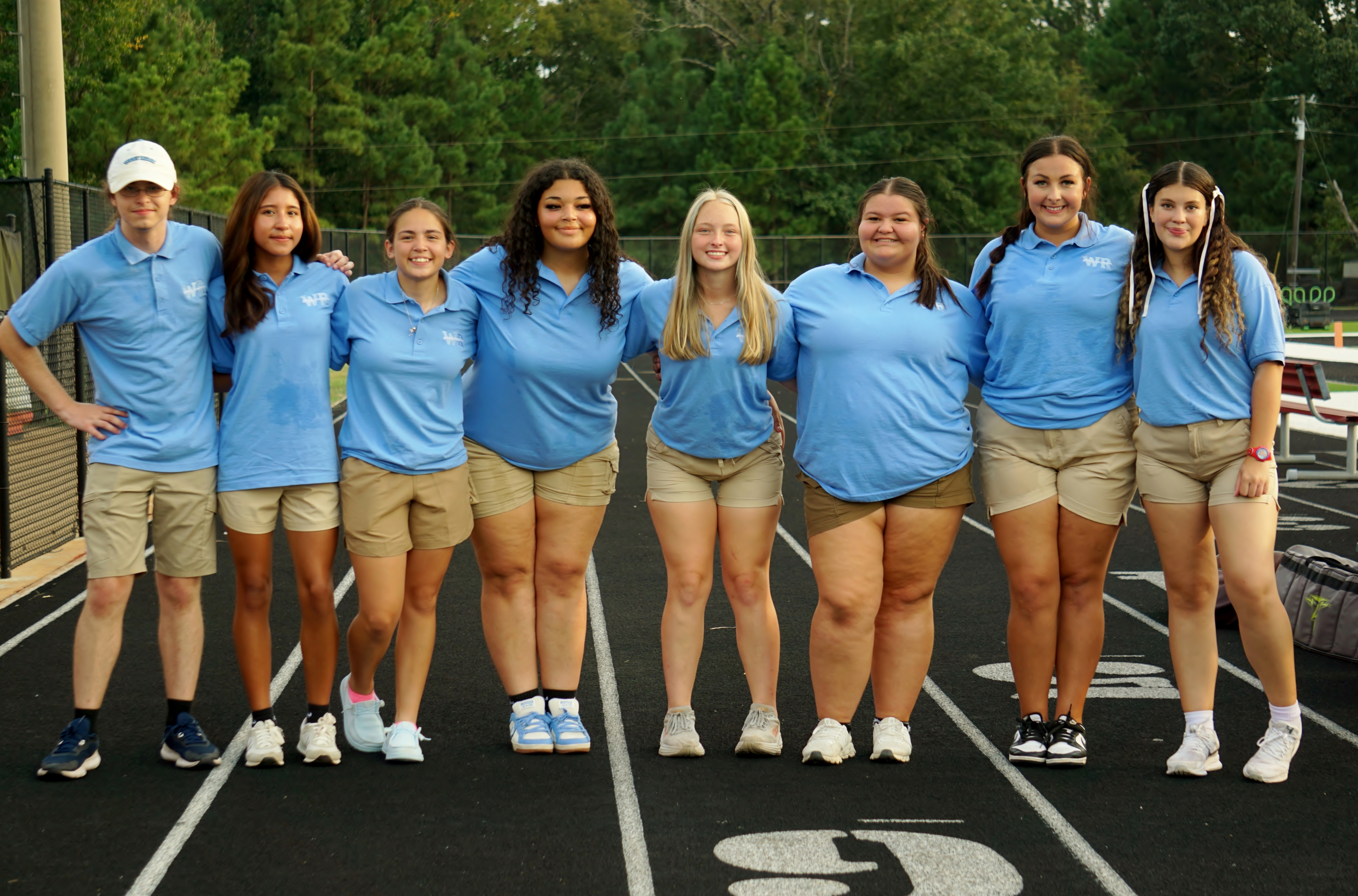 A group of young people, likely a sports team, standing together on a sports court surrounded by trees and other greenery.