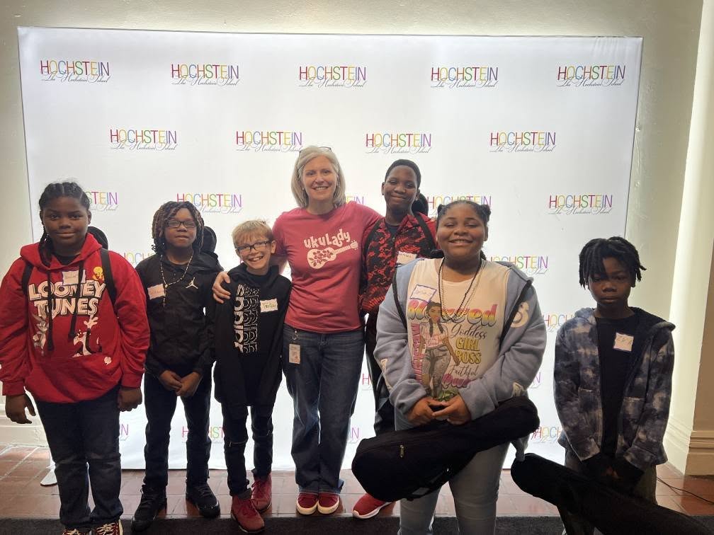 A group of people, including a woman in a red shirt, standing in front of a backdrop with the "H-STEIN" logo.