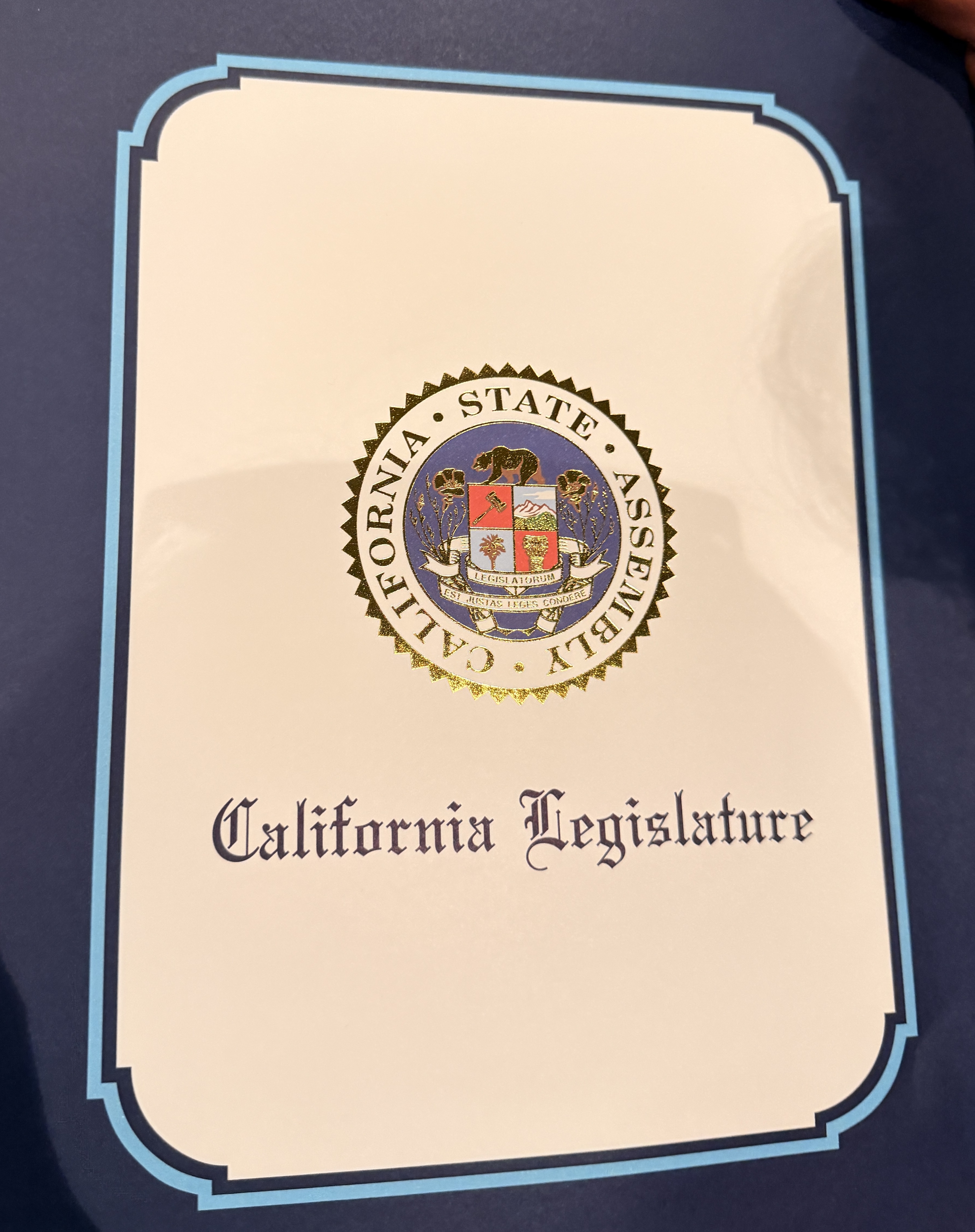 The image shows the seal of the California Legislature on a beige document with a blue border.