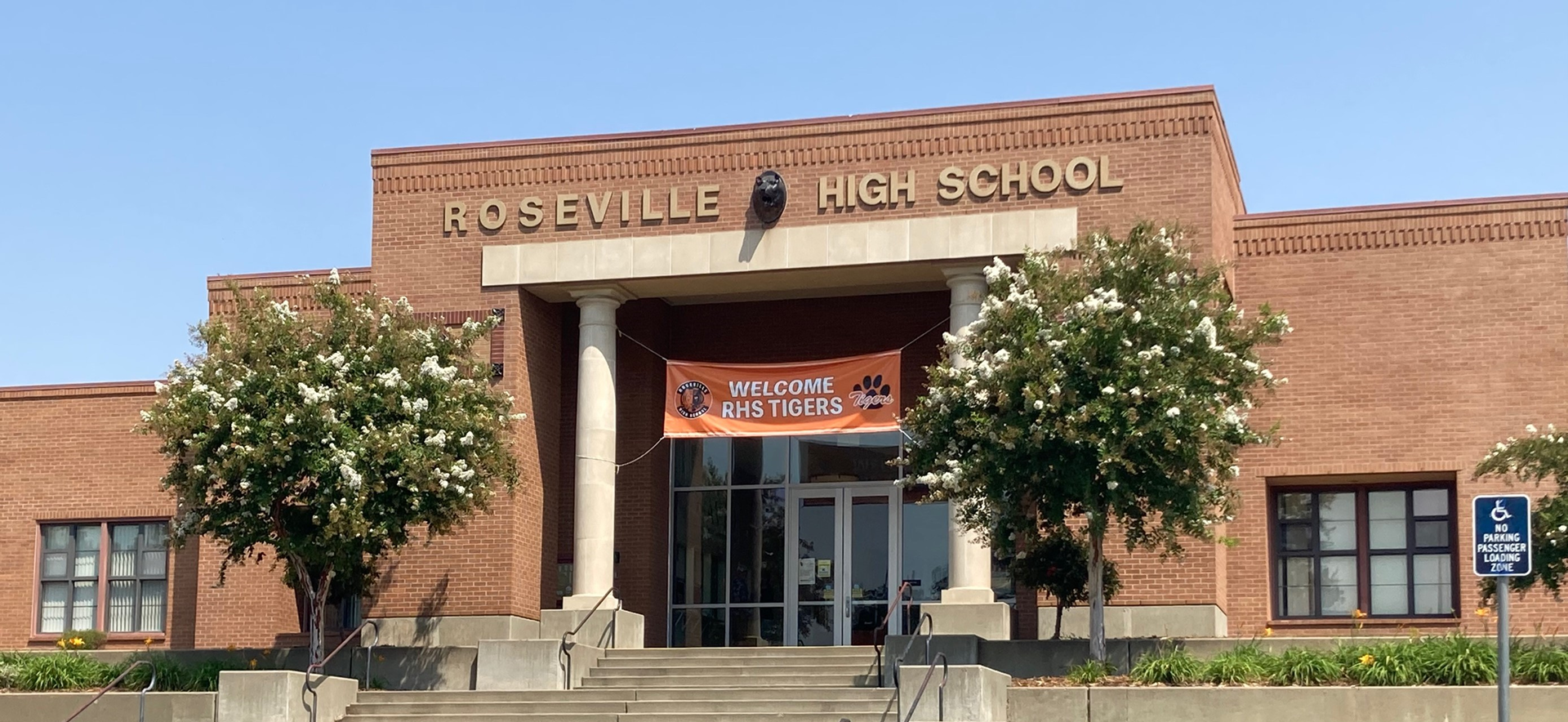 A brick building with the words "Roseville High School" prominently displayed above the entrance, surrounded by trees and a welcoming sign.