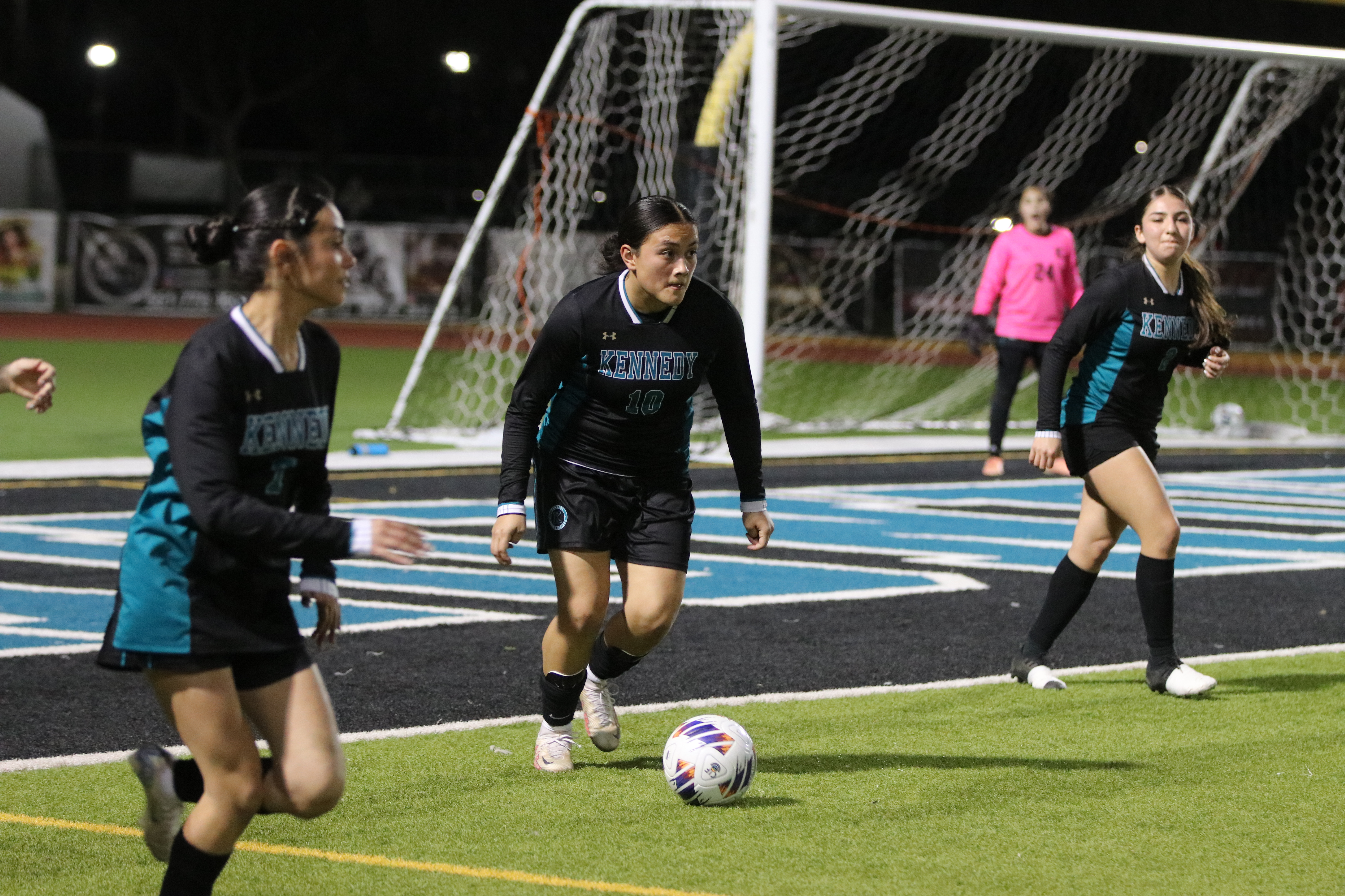 A group of people, likely soccer players, are on a soccer field at night, with the goal posts visible in the background.