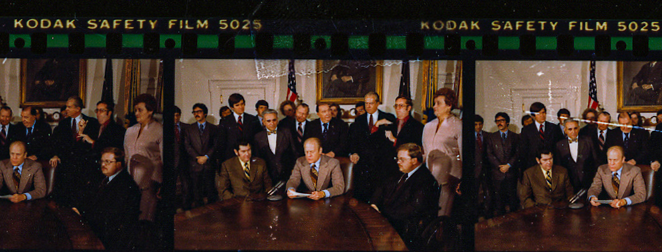 This is a photo from a Kodak photo reel of President Gerald R Ford, sitting at a table in the White House cabinet room, surrounded by over a dozen special education advocates. Circa November 1975.