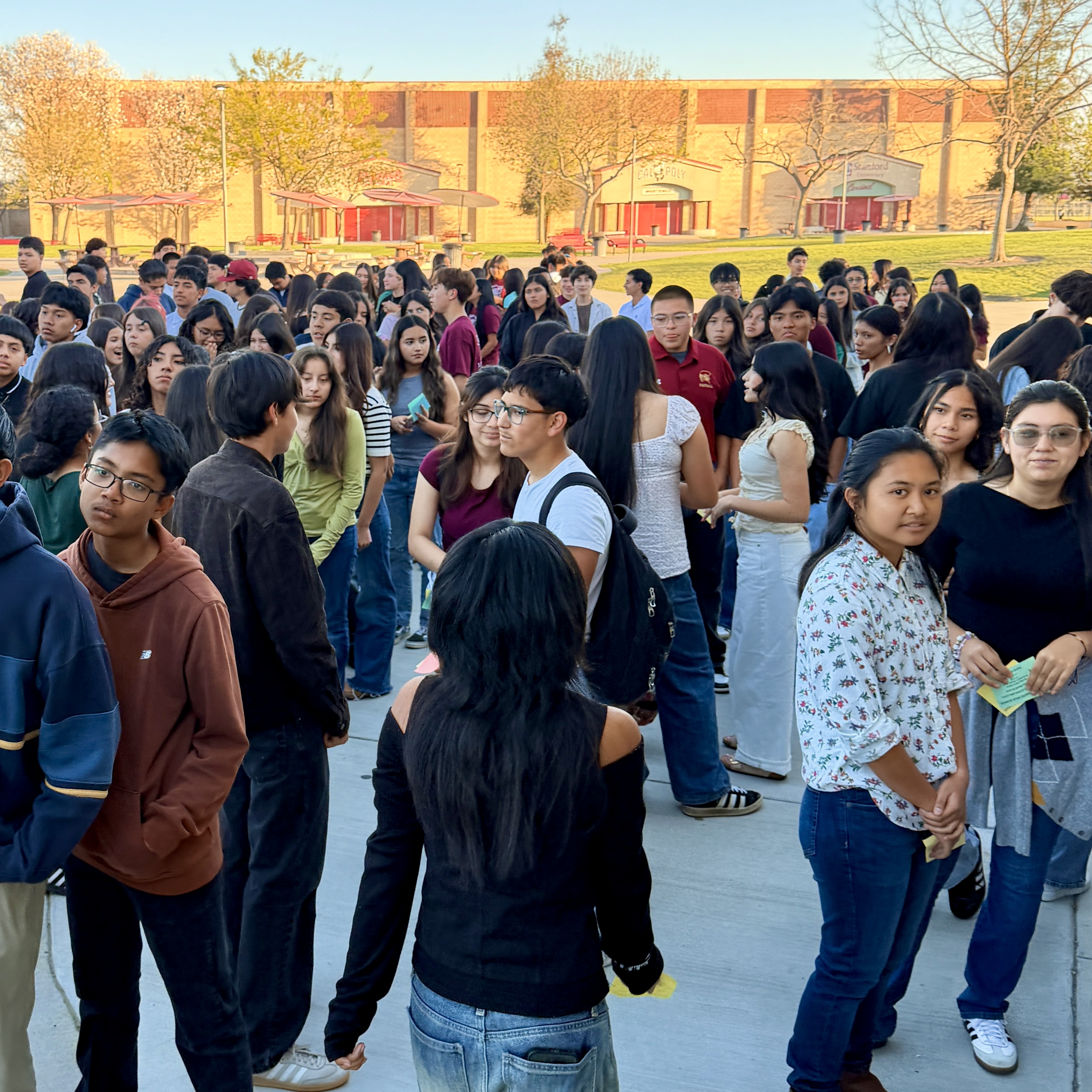 A large crowd of students, mostly young people, gathered in an outdoor setting with a brick building in the background.