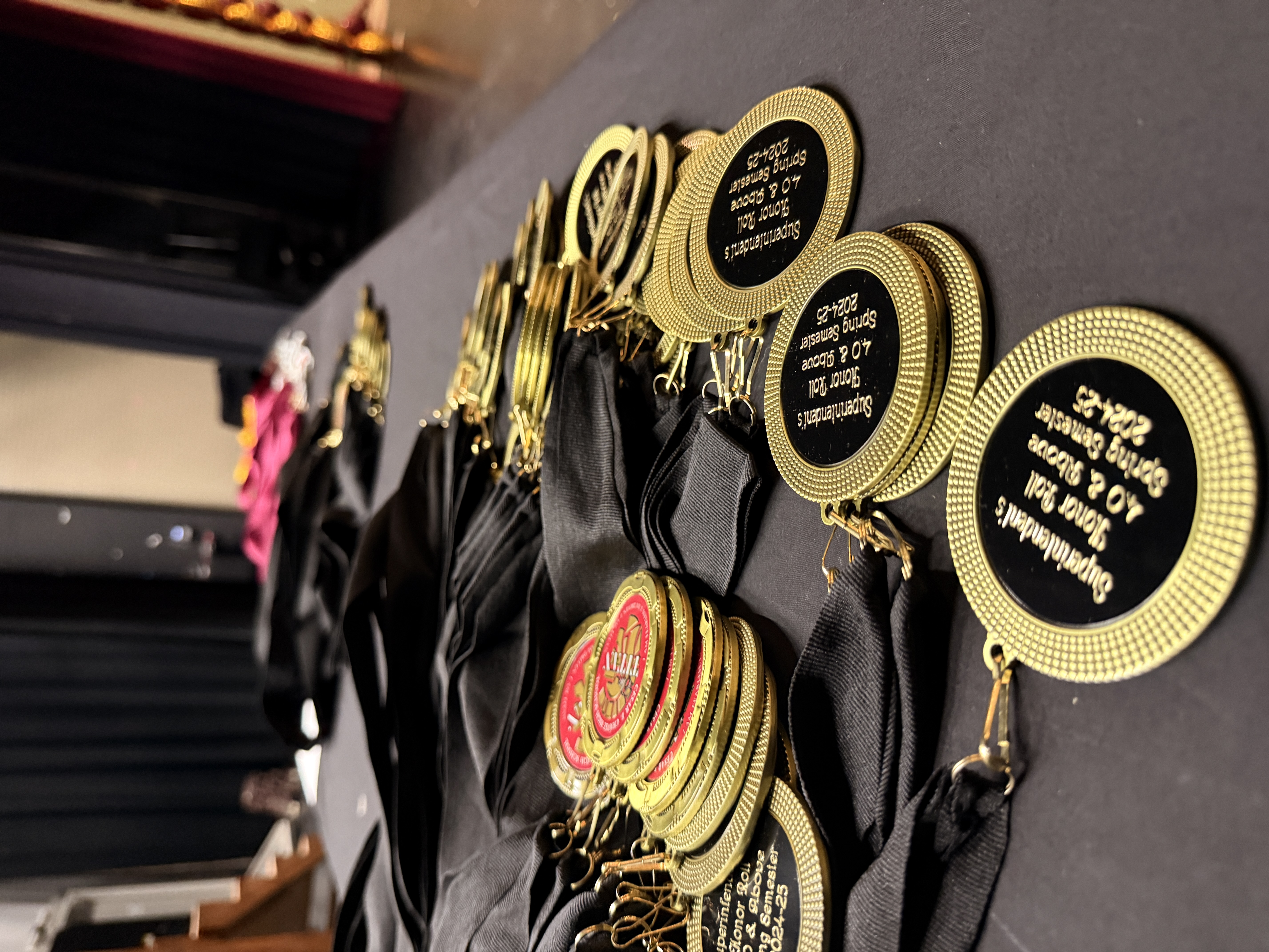 A collection of gold-colored medals or awards with the text "1st" on them, arranged on a black background with various other items.
