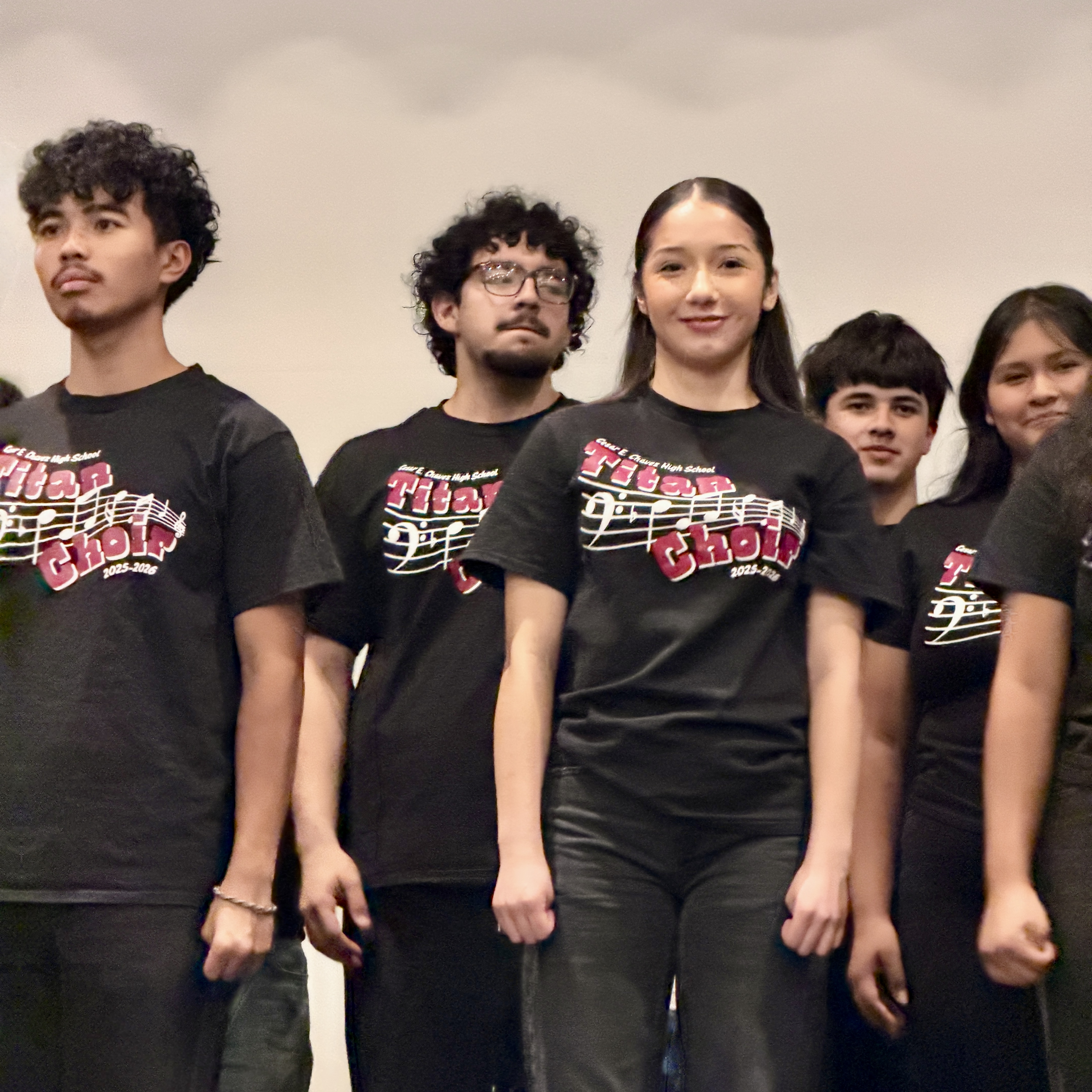 A group of young people, wearing matching black t-shirts with a graphic design, stand together against a plain background.