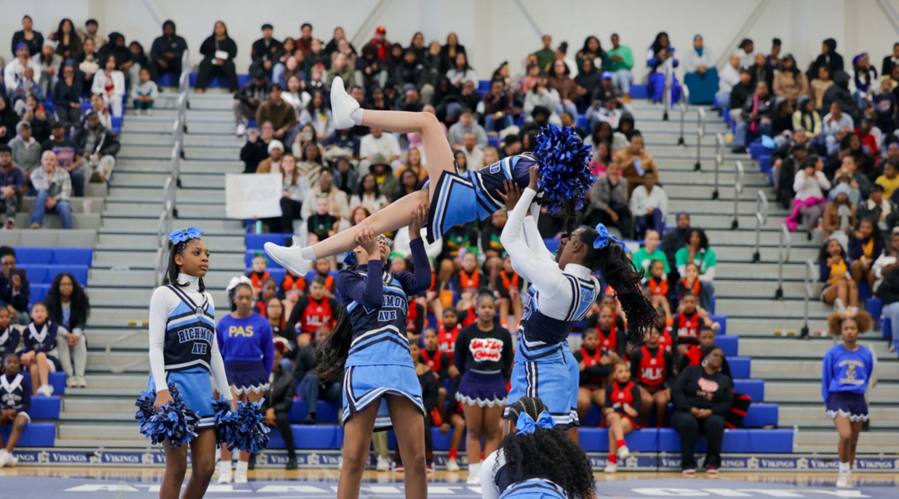 A group of cheerleaders performing acrobatic stunts on a stage in front of a large crowd of spectators.