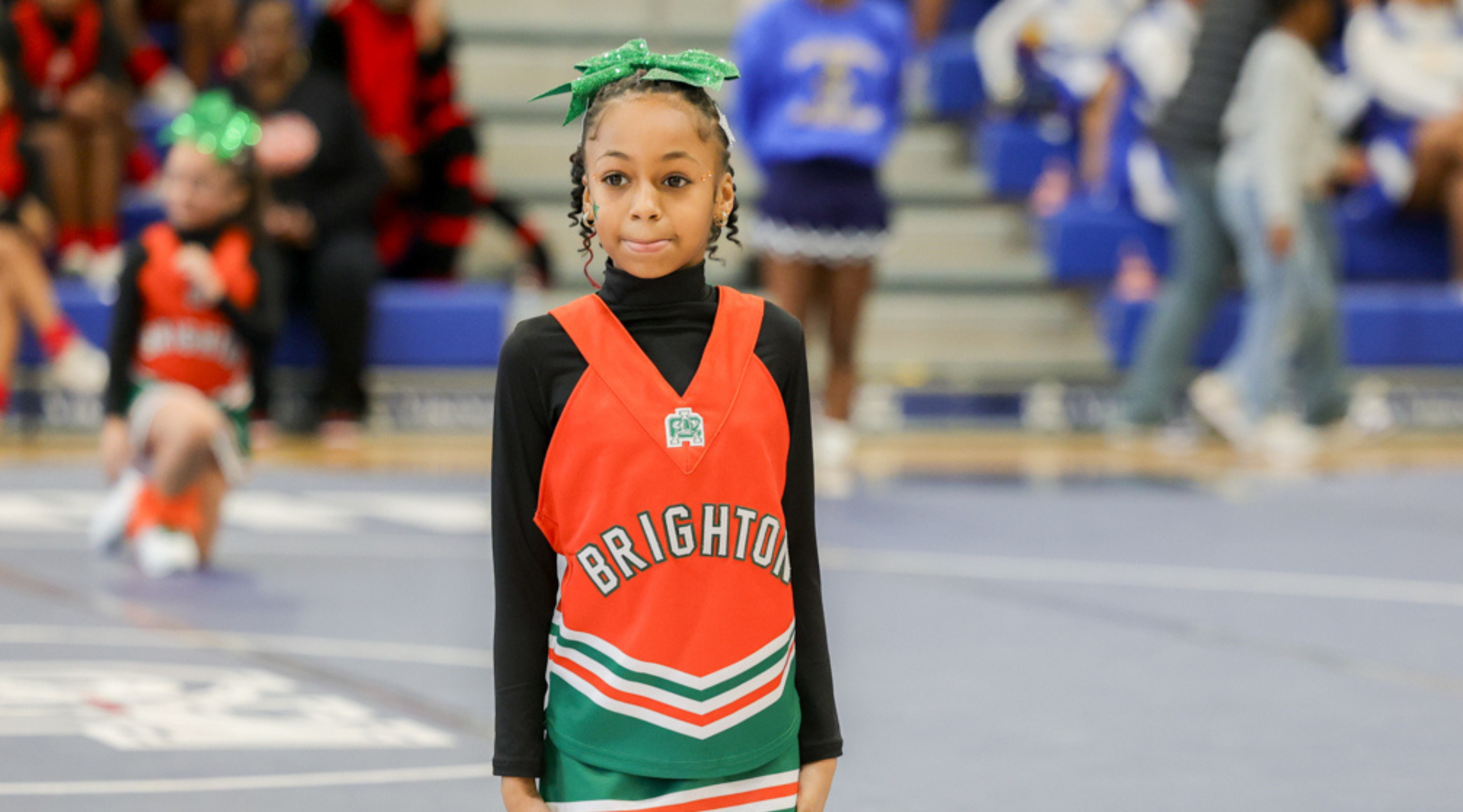 A young person wearing a bright red and green sports jersey stands in the foreground, surrounded by other people in the background.