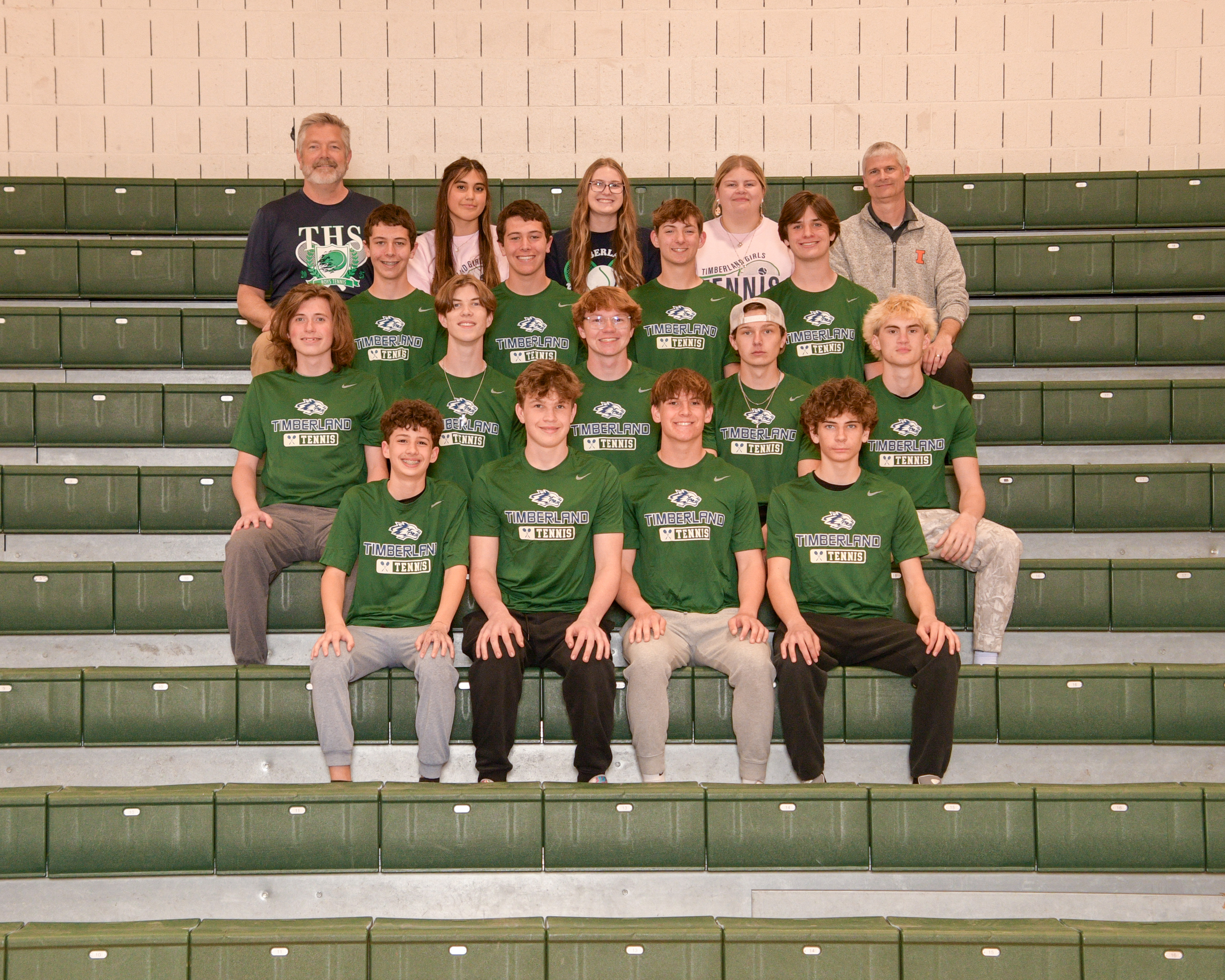 A varsity tennis team, posing together on stadium seating with green and gray colors in the background.