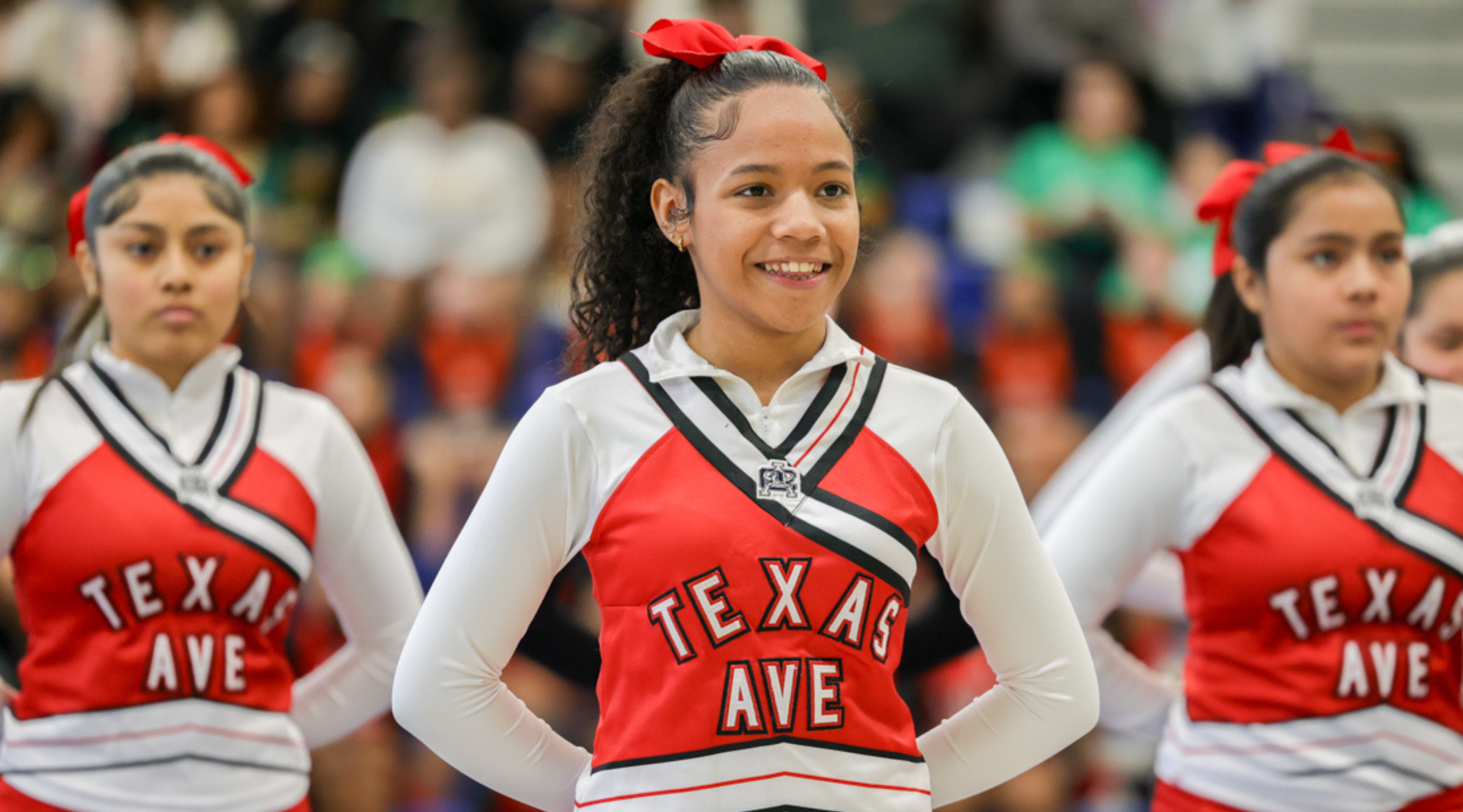 The image shows a group of young women wearing cheerleader uniforms with "Texas Ave" printed on them, standing together and smiling.