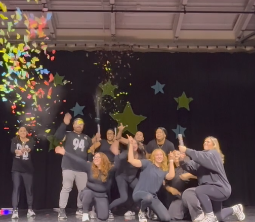 A group of people in casual clothing posing together in front of a dark background with colorful stars and lights.