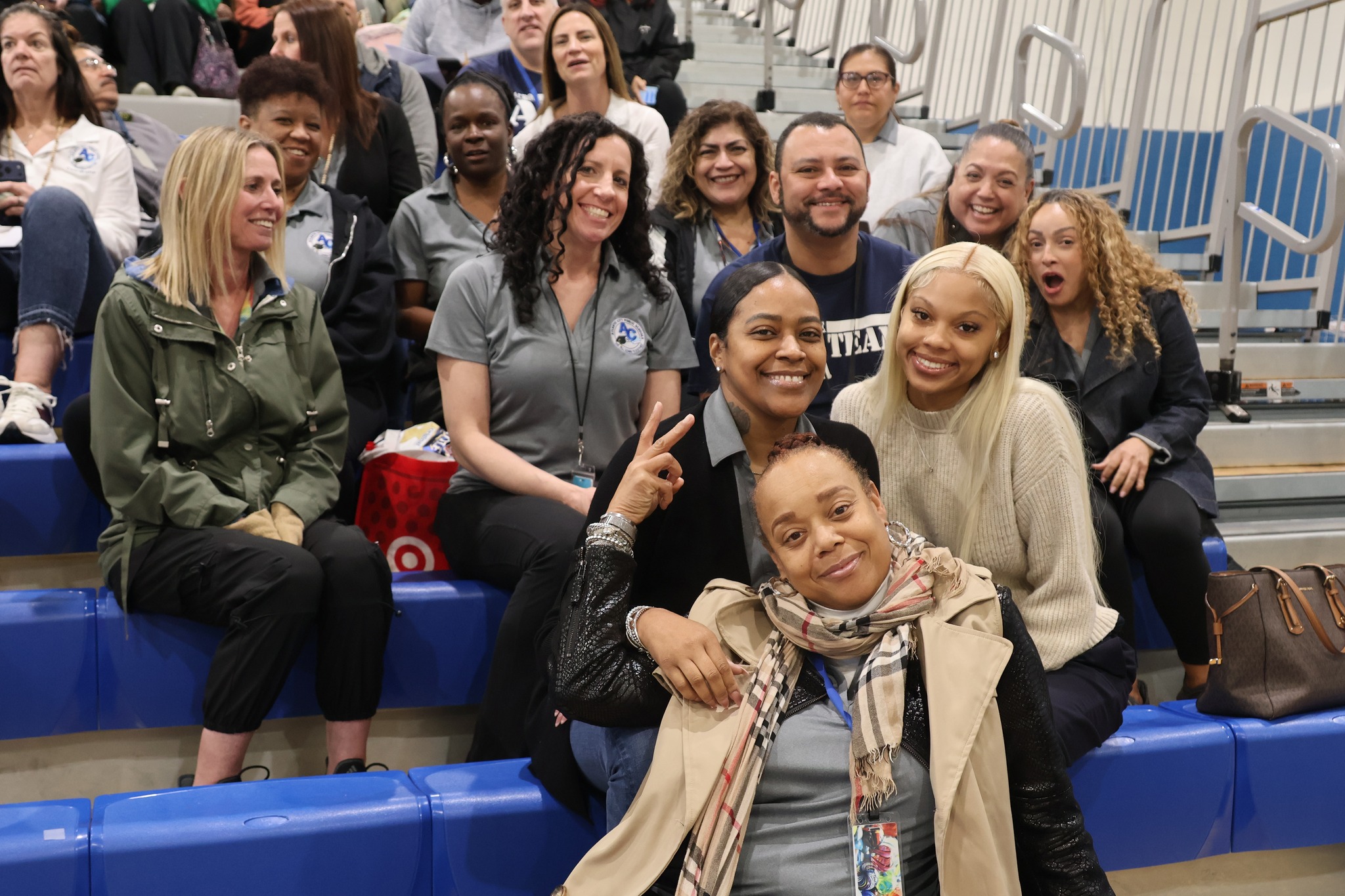 A group of diverse individuals, including men and women of various ages and ethnicities, are gathered together and appear to be engaged in a social or professional event, with a backdrop of what seems to be a stadium or arena setting.