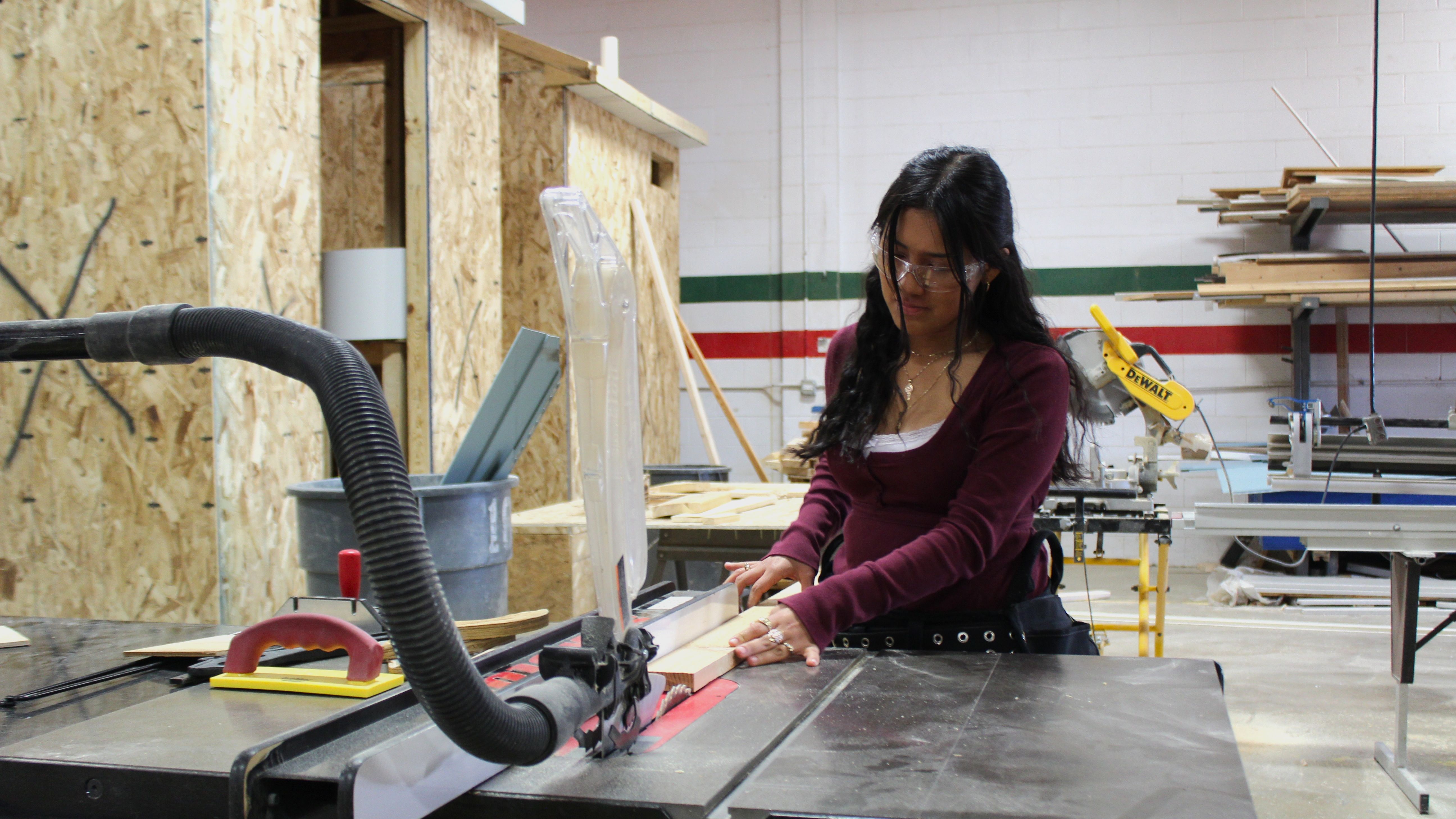 a Construction student is trimming the size of a piece of wood using power tools