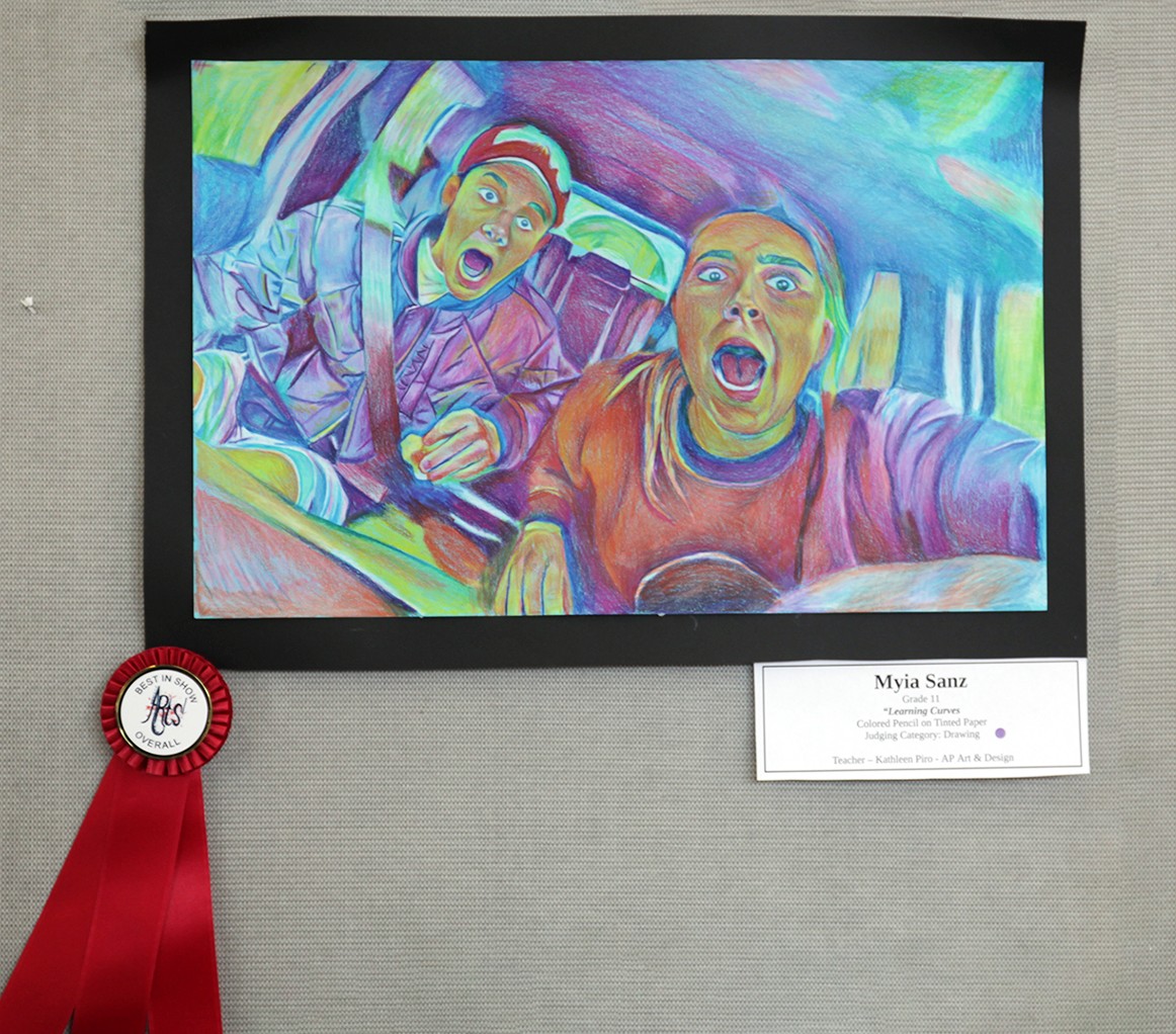 Two people with wide-eyed expressions are captured in a colorful, abstract interior, possibly a car, with a red ribbon and award label below.