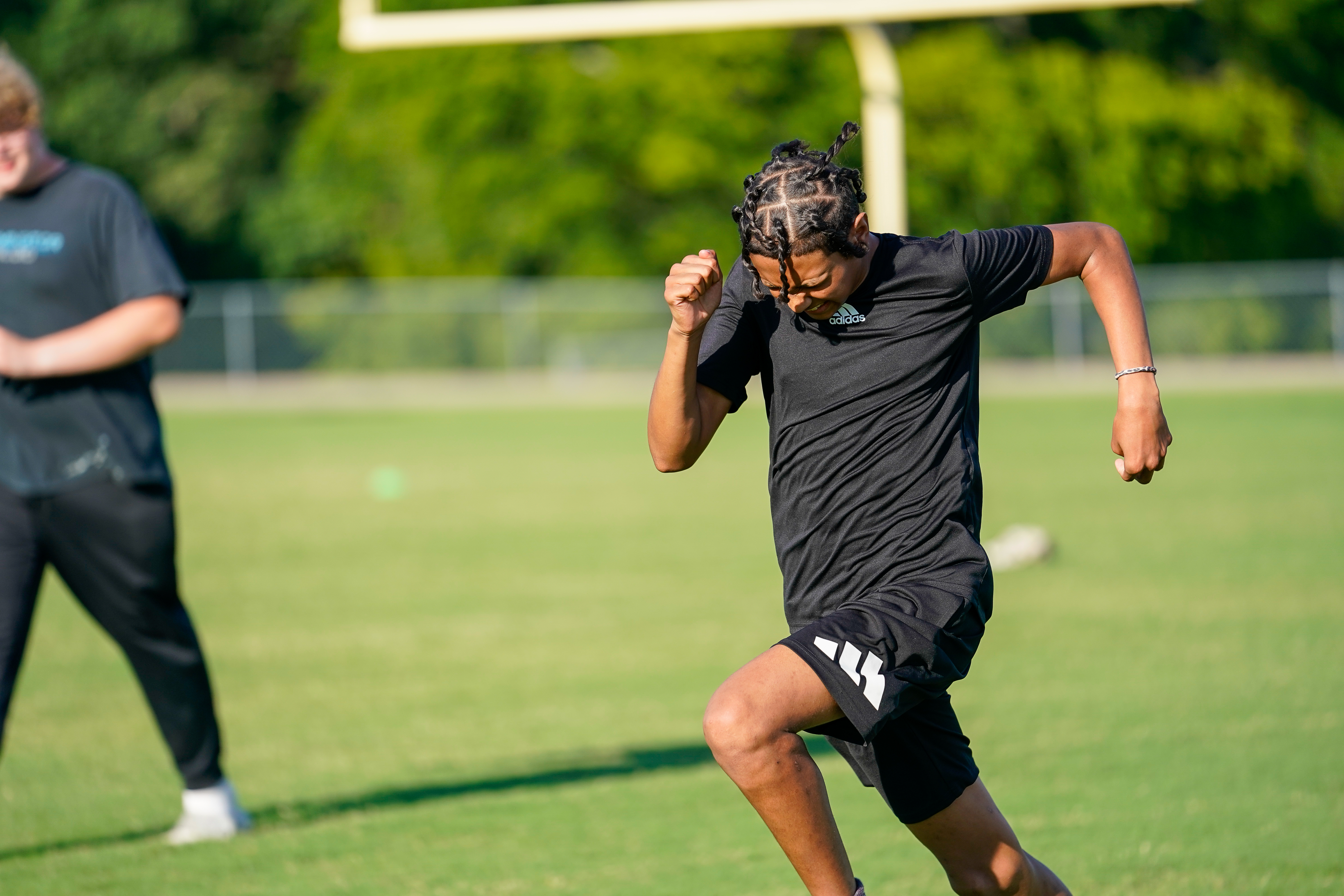 A young man in athletic wear sprints across a grassy field with a goalpost visible in the blurred background.