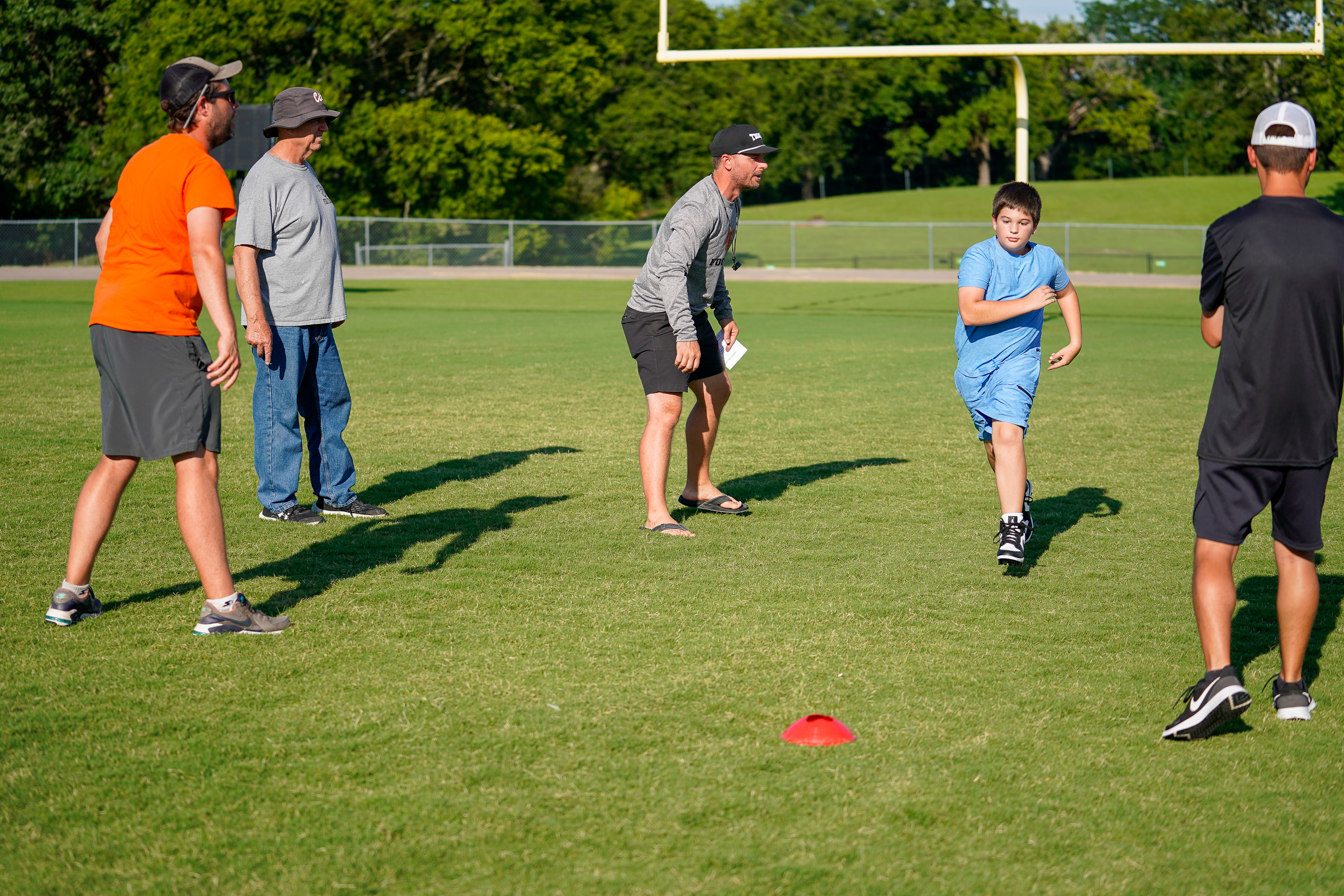 A group of men and a boy stand on a grassy field with a football goalpost in the background.