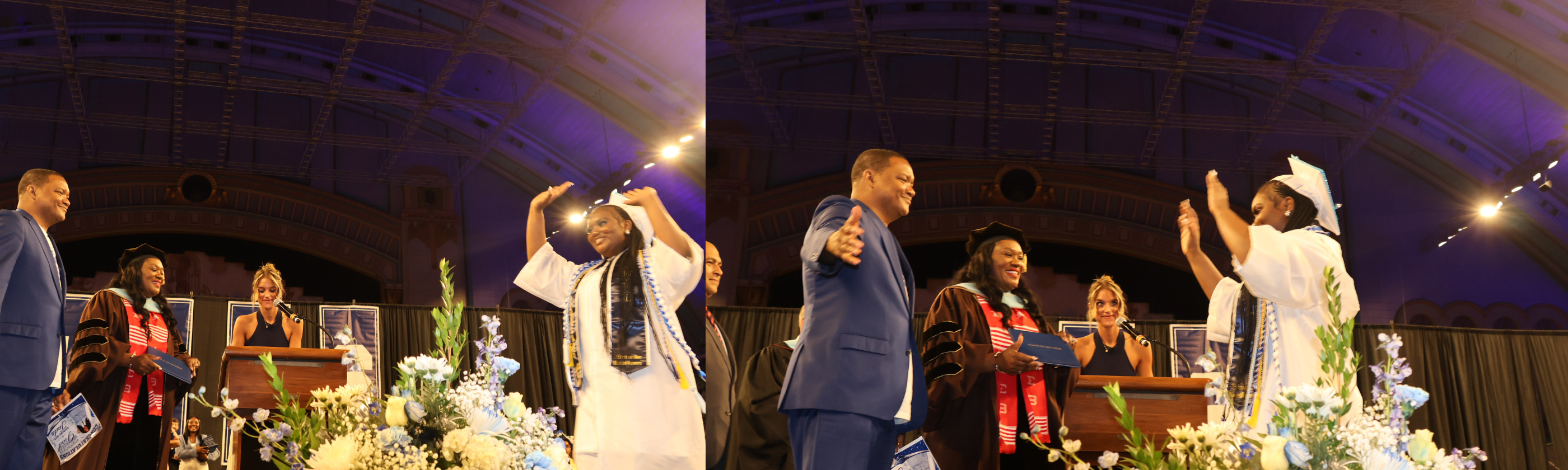 A graduate in a white cap and gown celebrates on stage with floral arrangements in the foreground, while a man in a suit and other attendees are visible in the background under a large, arched ceiling.