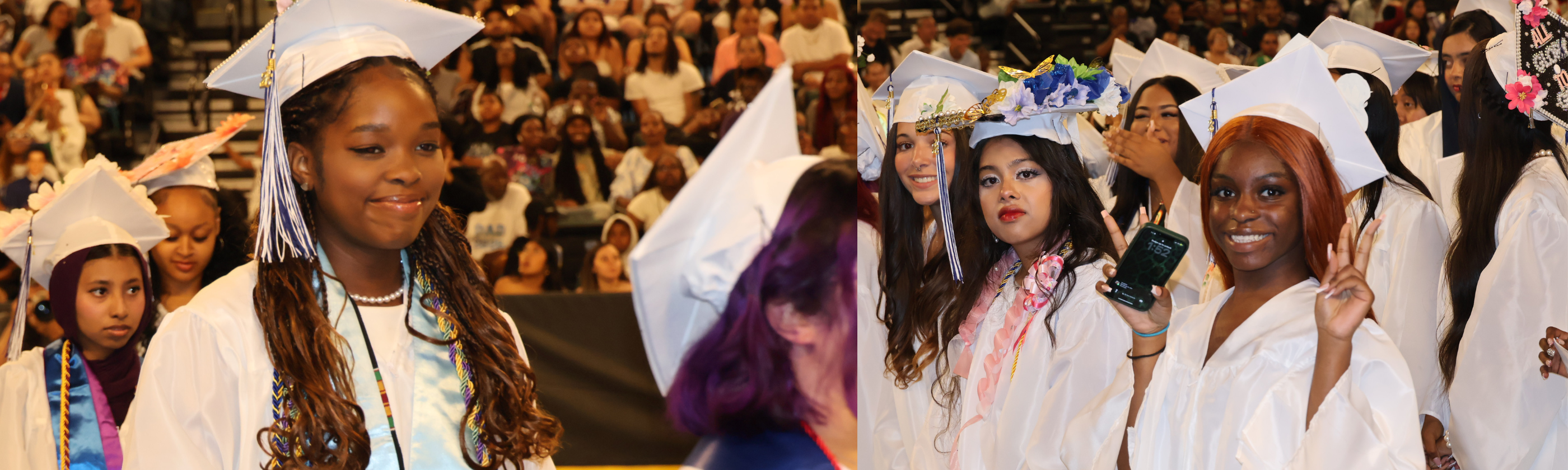 Graduates in white gowns and caps stand in the foreground, while an audience fills the blurred background.