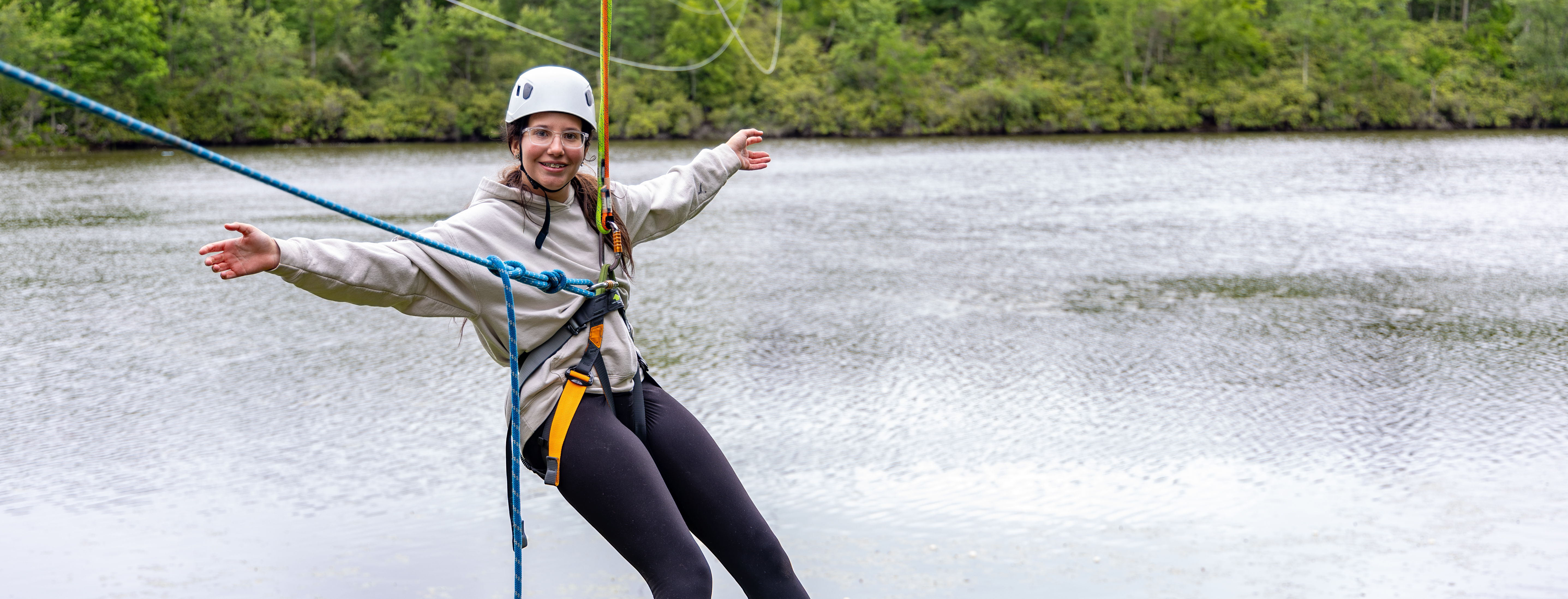 A girl smiles for a photo after finishing a zipline over a lake.