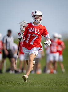 A lacrosse player in a red jersey with "WALL 17" on it runs on a green field with other players blurred in the background.
