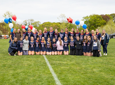 A group of young women in matching uniforms pose for a photo on a grassy field with balloons in the background.