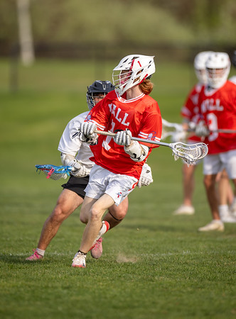 A lacrosse player in a red jersey runs with his stick on a grassy field, while other players in red and white uniforms are visible in the blurred background.
