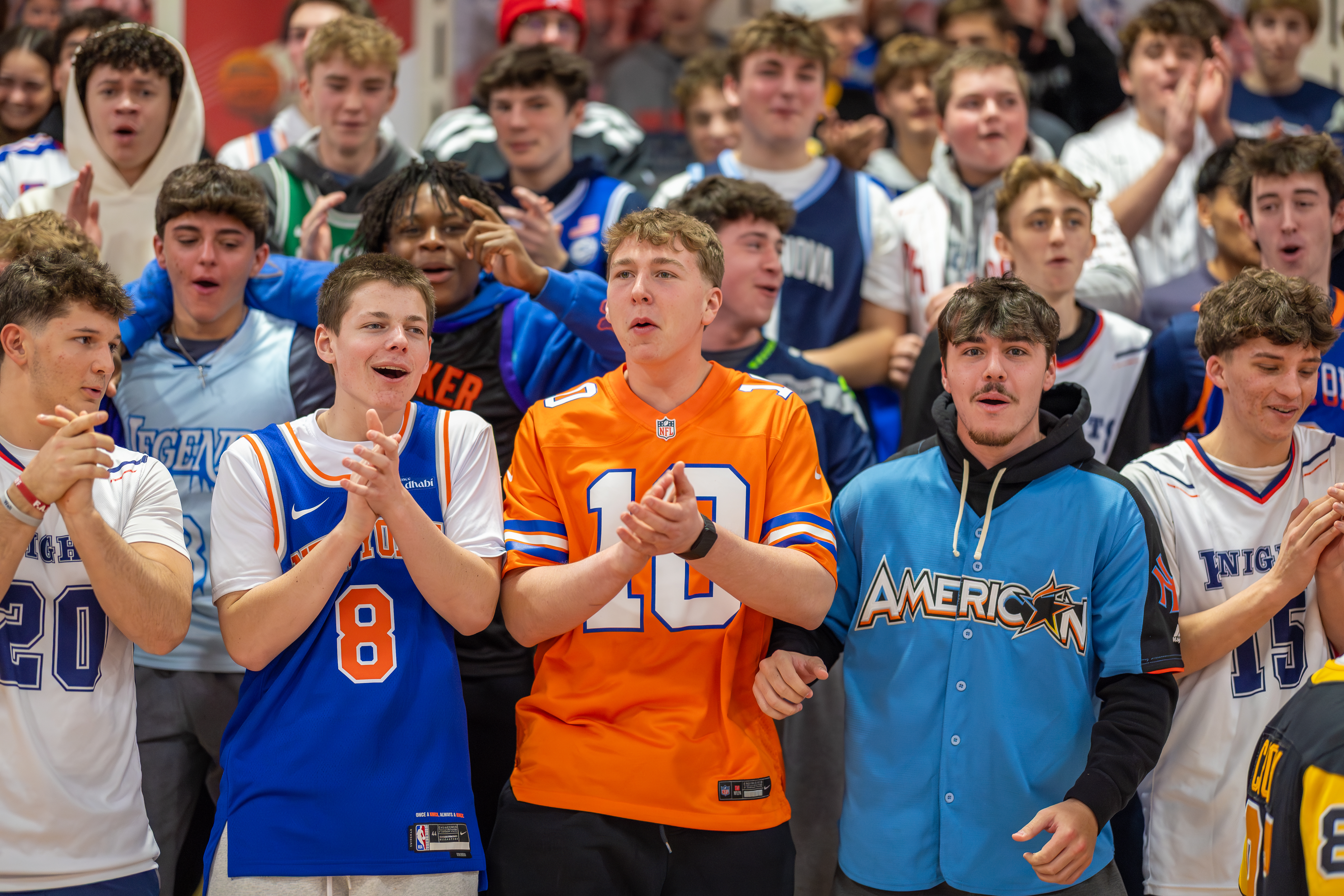 A group of excited young fans in the foreground cheer at a sporting event, with a blurred crowd in the background.