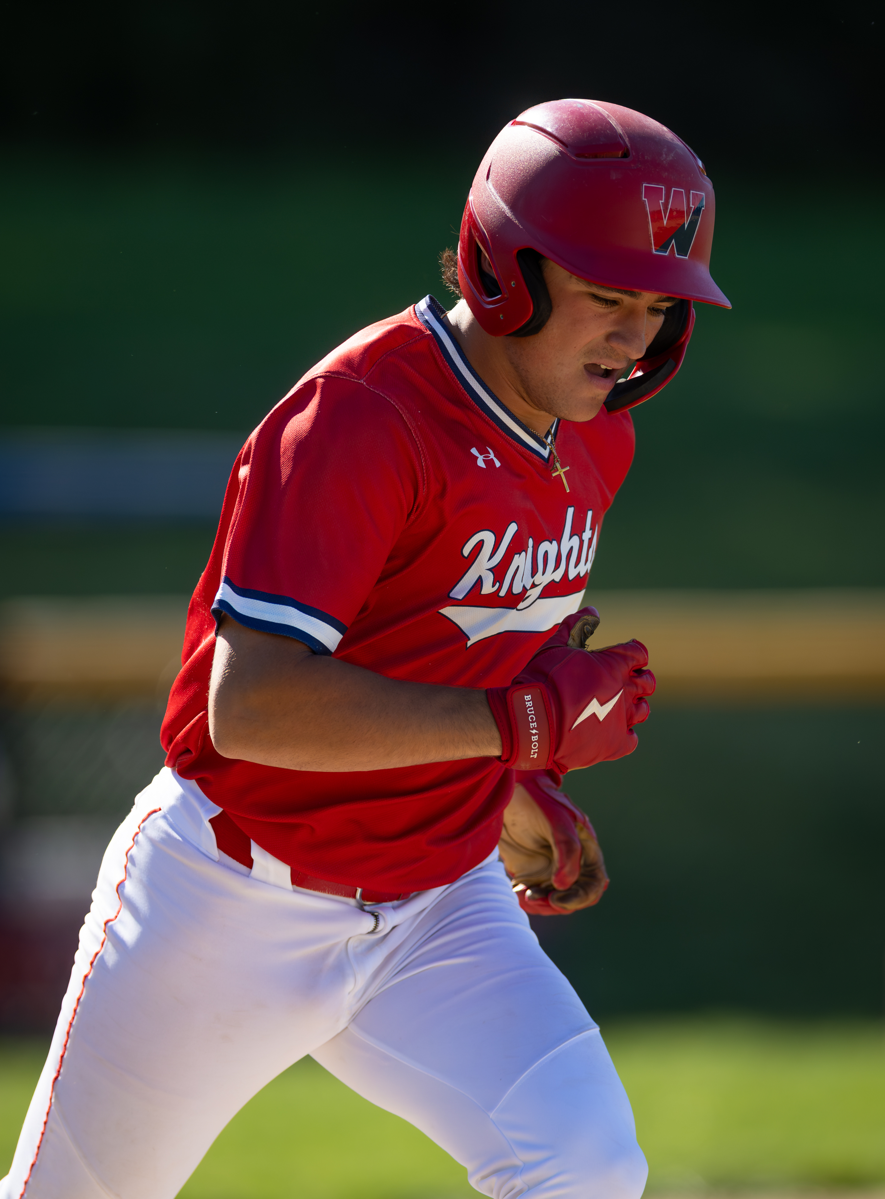 A baseball player in a red uniform with white pants runs on a field with a blurred green background.