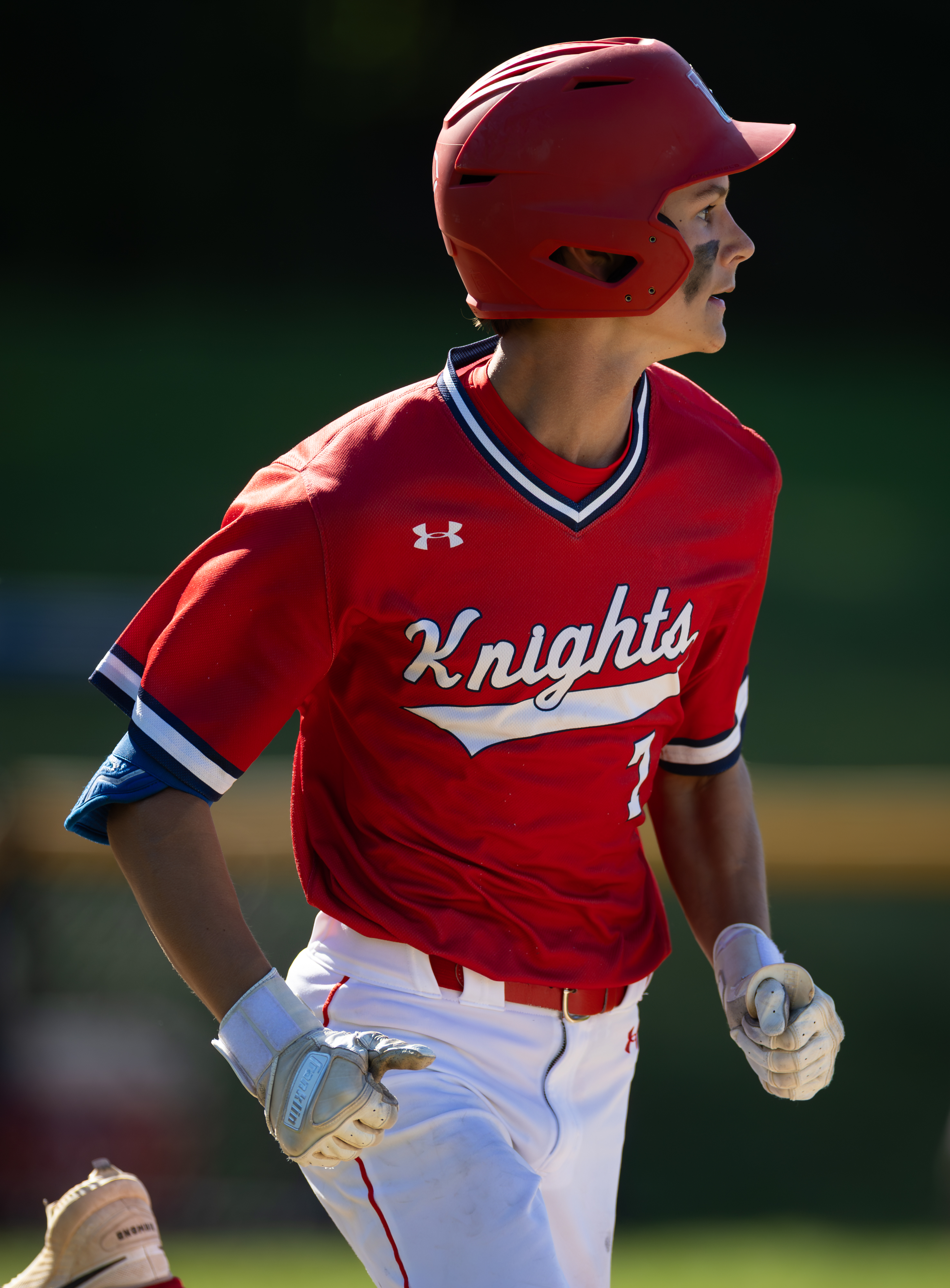 A young baseball player in a red Knights uniform runs on a field with a blurred green background.