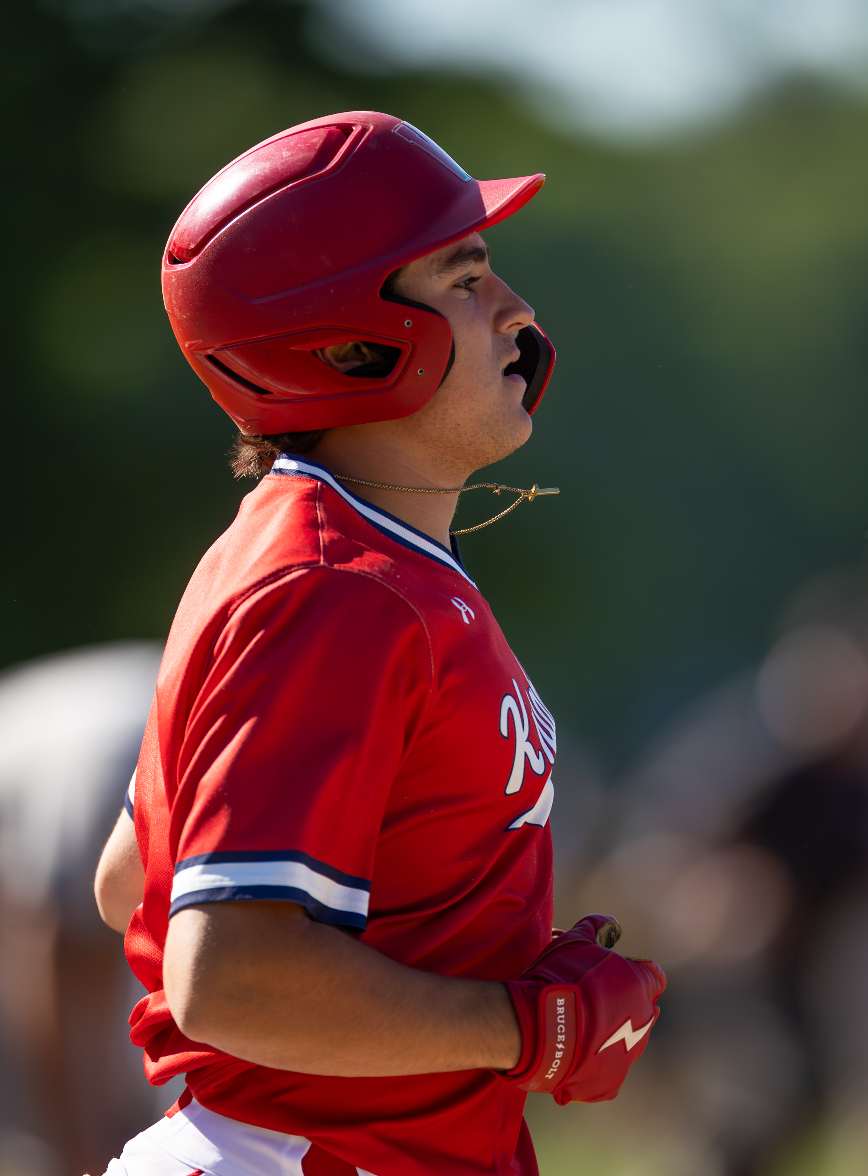 A young baseball player in a red uniform and helmet runs with a blurred green background.