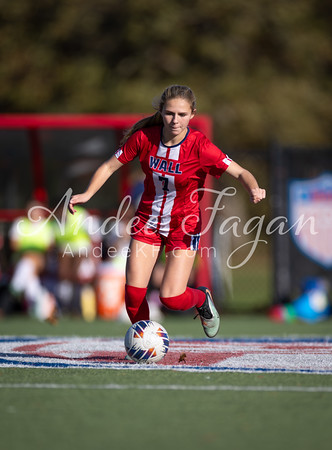 A young woman in a red soccer uniform dribbles a ball on a field with a blurred background of spectators and a stadium.