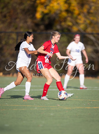 Two young women in soccer uniforms are playing on a field with trees in the background.