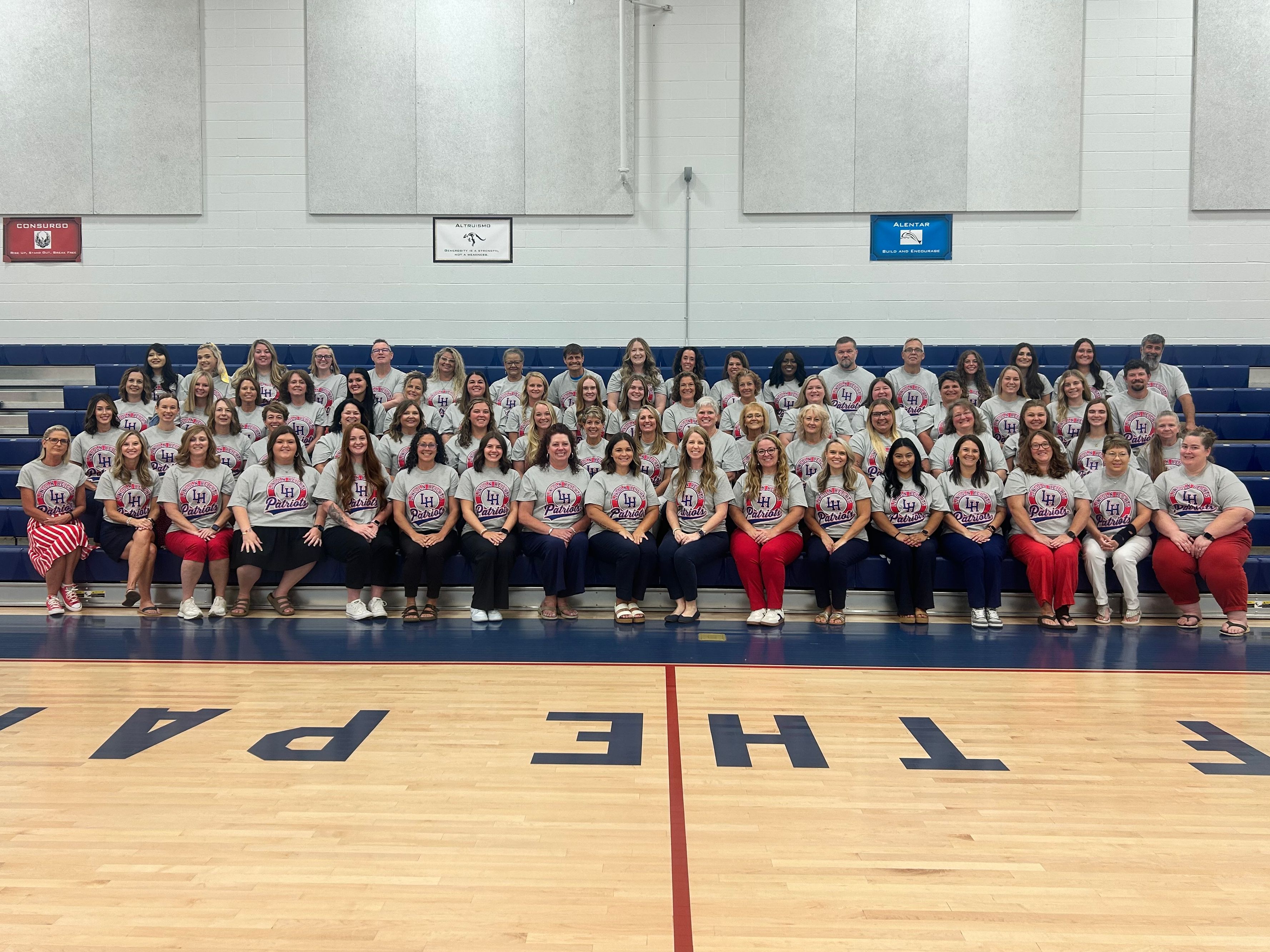 A large group of staff pose on bleachers in school gym.