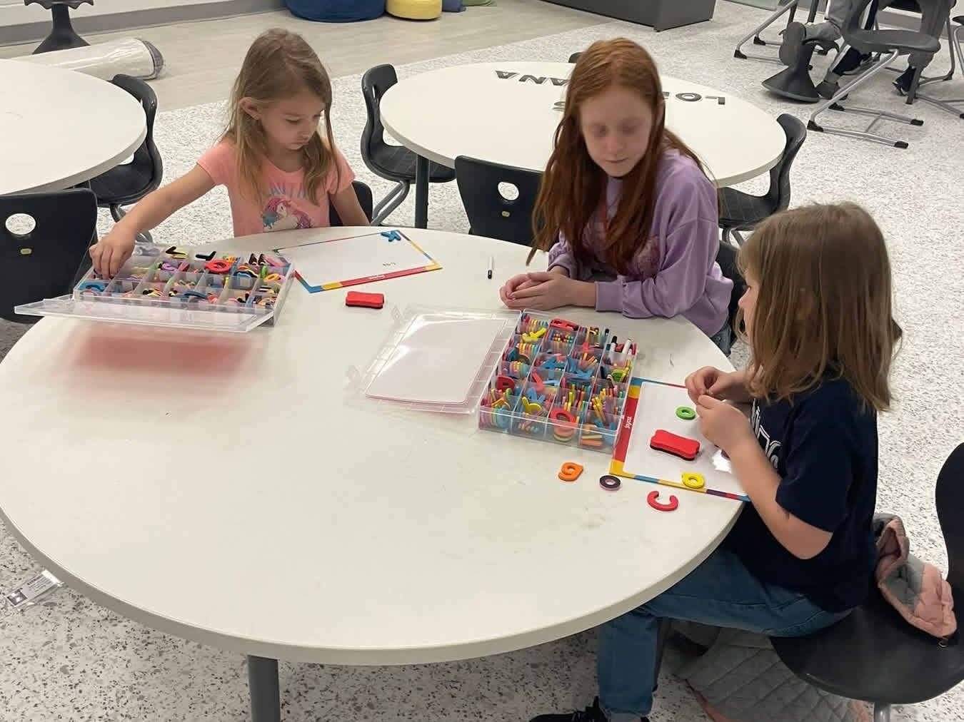 An older student helps two younger students in a classroom.